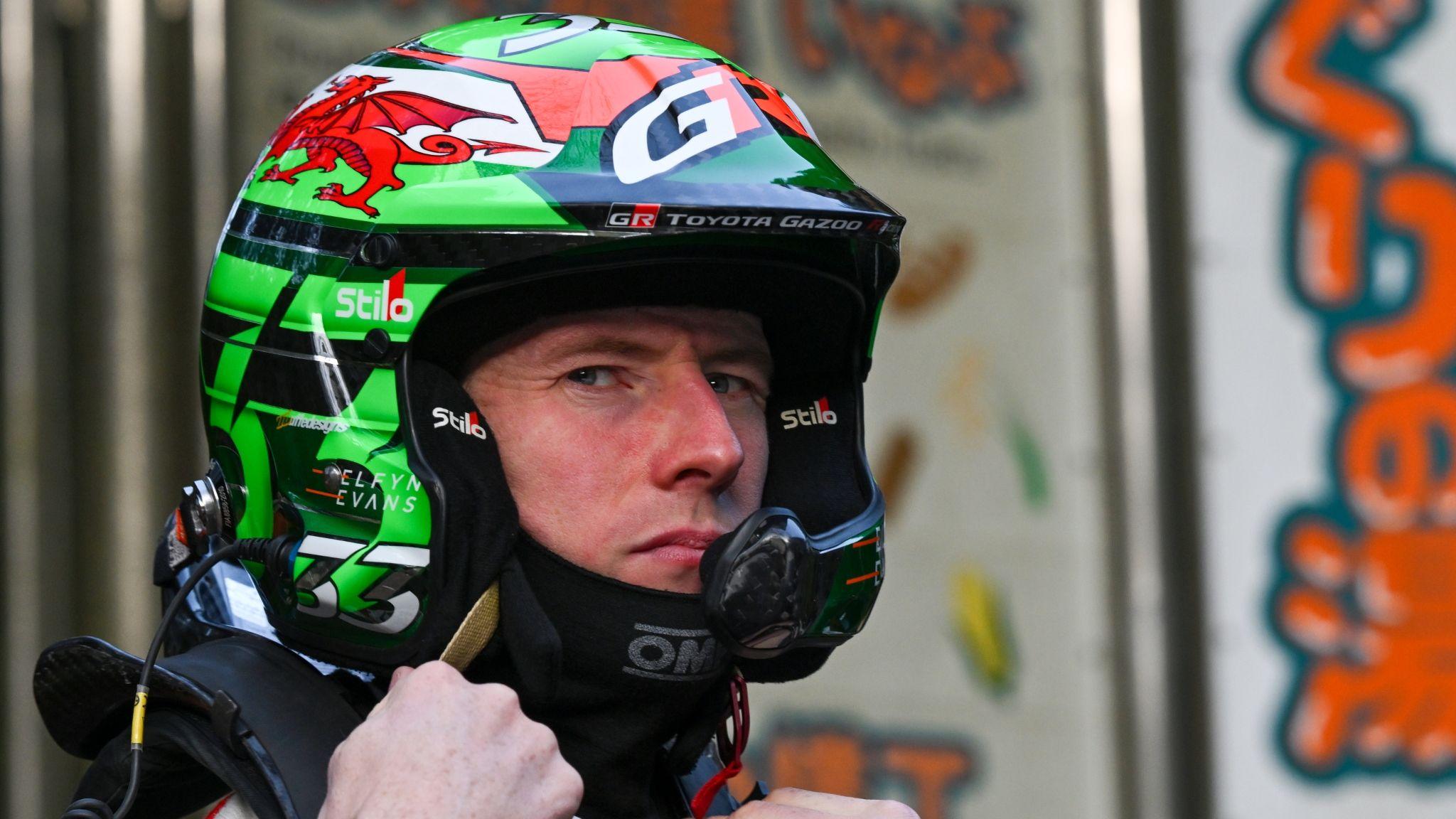 Elfyn Evans stares sideways into the camera while wearing a motor racing helmet decorated with the Welsh flag