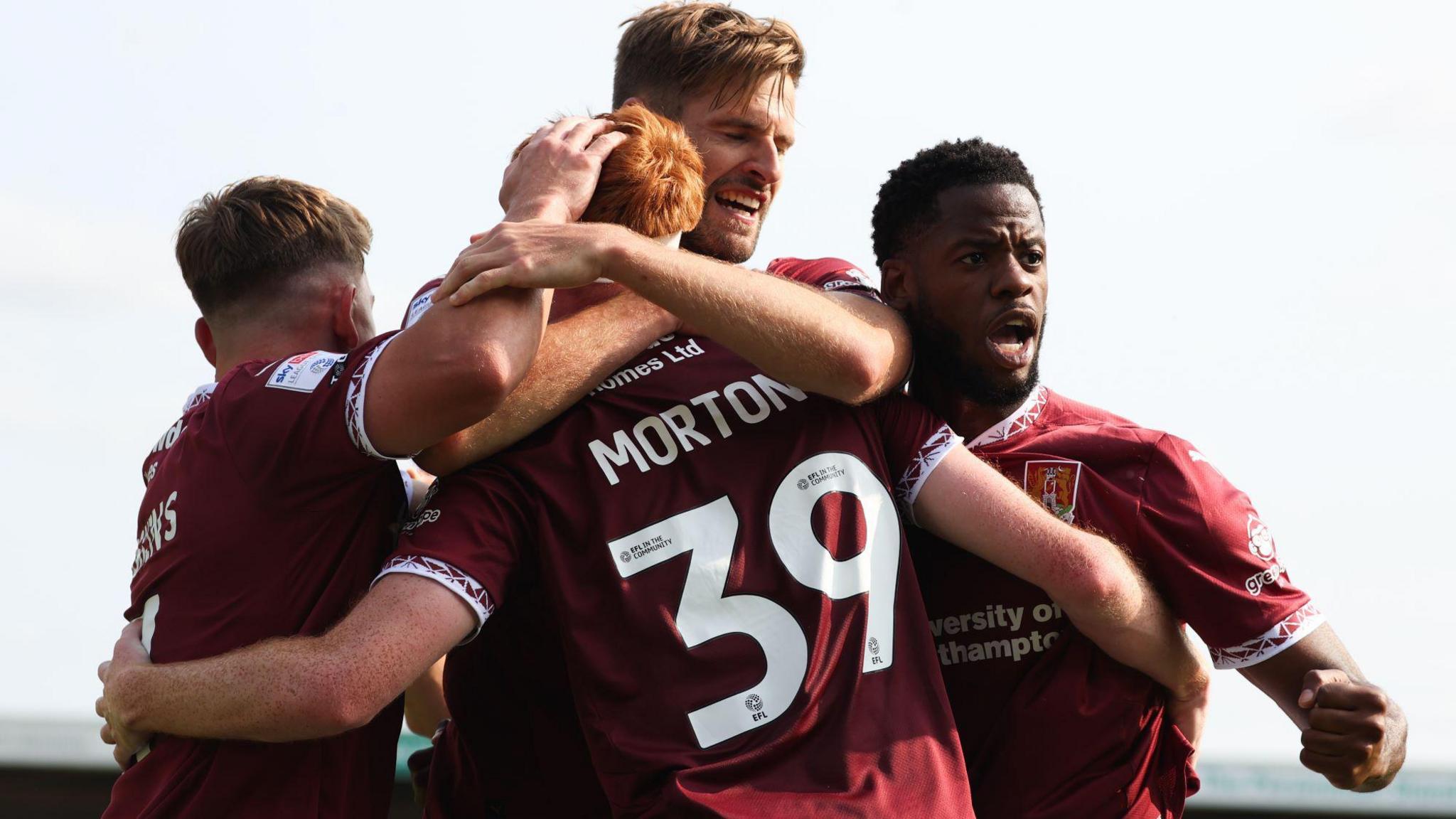 Northampton Town's Callum Morton celebrates with Sam Hoskins, Jon Guthrie and Luke Mbete during a League One match at Sixfields Stadium, Northampton, in August. They are wearing a claret kit and Morton and Mbete have their mouths open while celebrating. The other two have their backs to the camera.