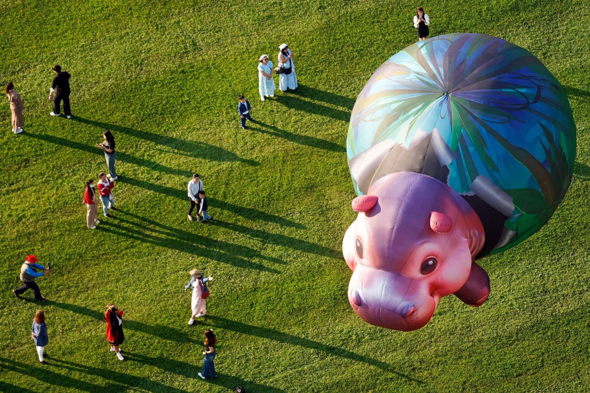 A baby hippo balloon is watched by visitors to a balloon festival