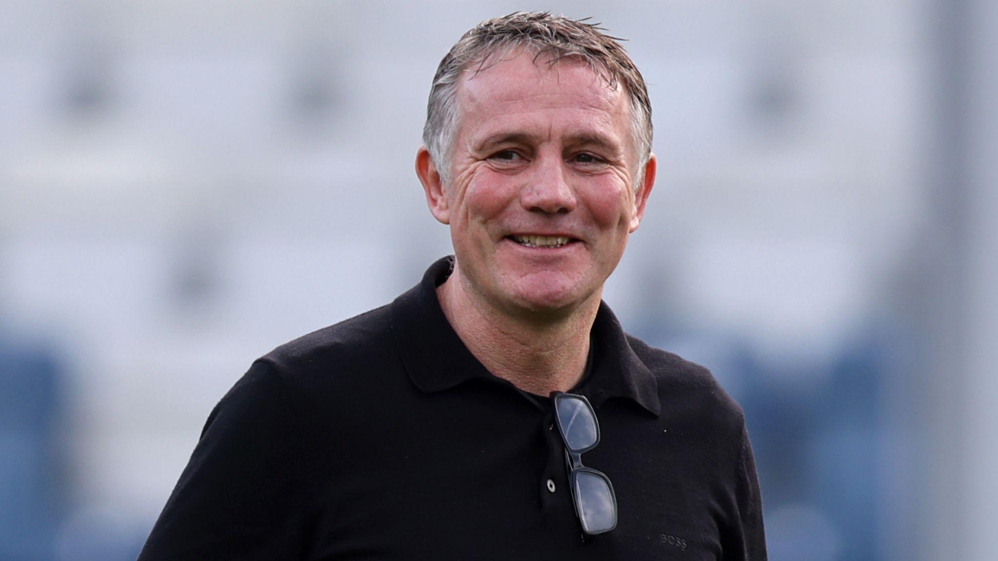 A smiling Wrexham manager Phil Parkinson wearing a black shirt with spectacles hooked over collar