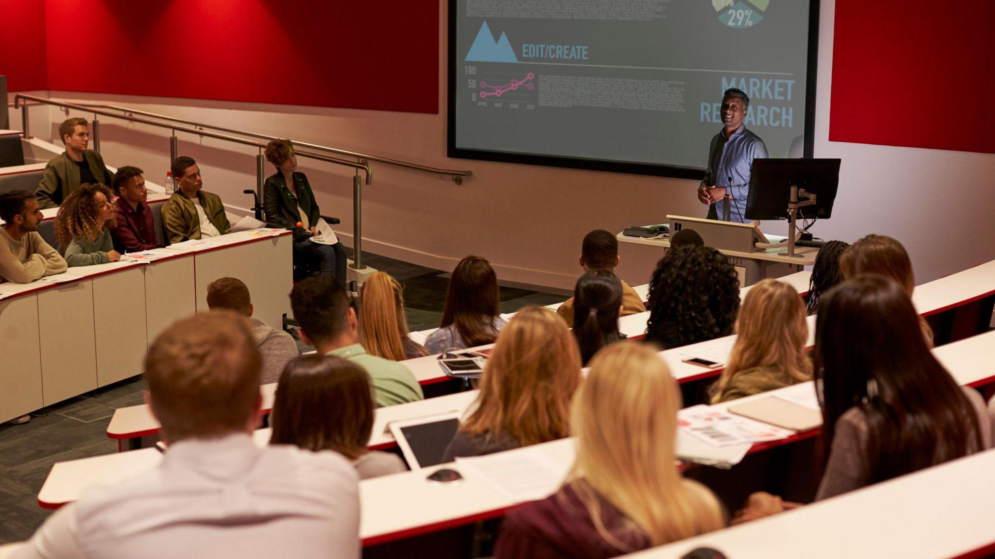 A lecture theatre full of students listen to a presentation by a professor at a university. 