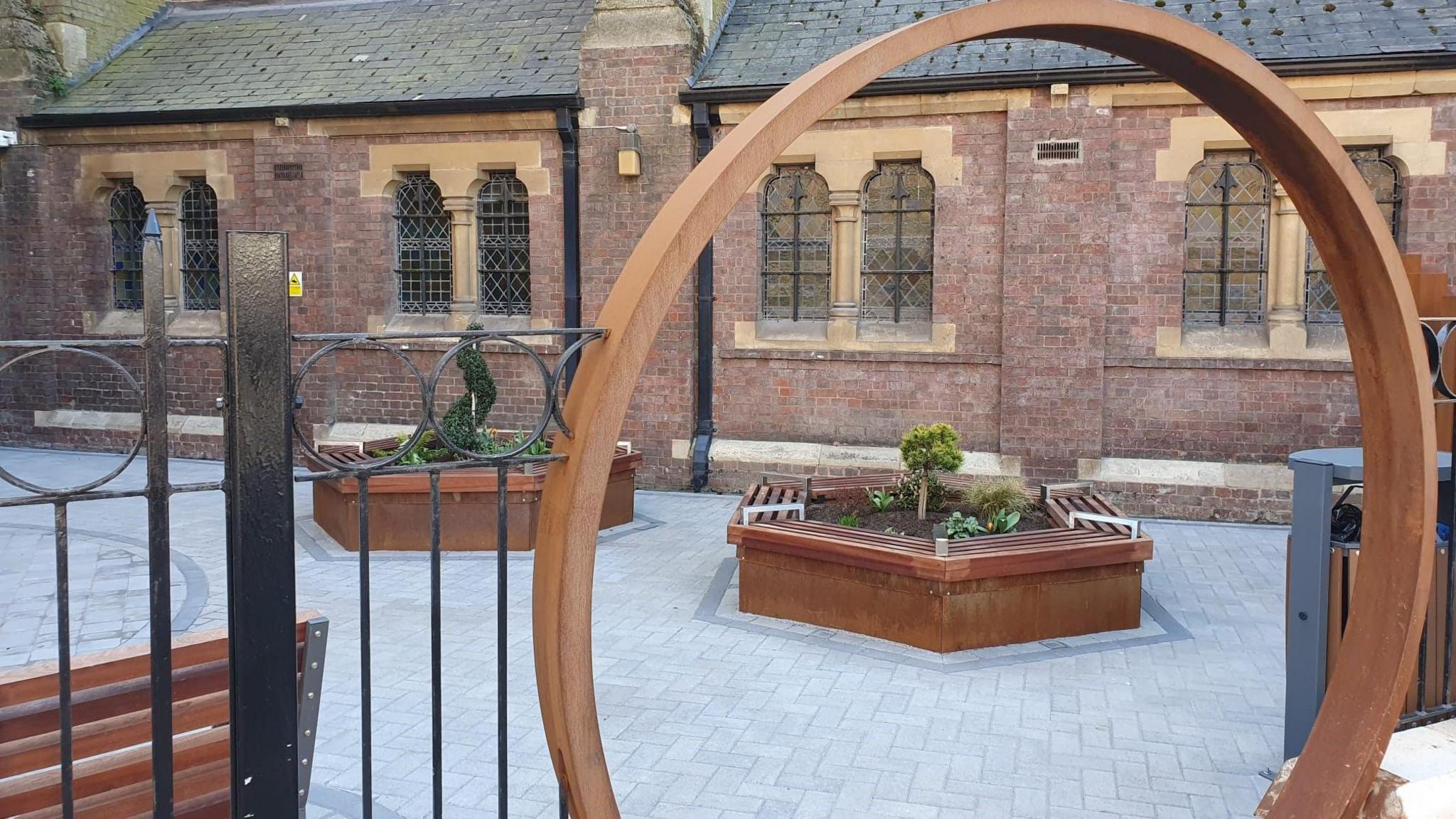 Wooden arch, revealing a garden in front of a church with planted raised beds