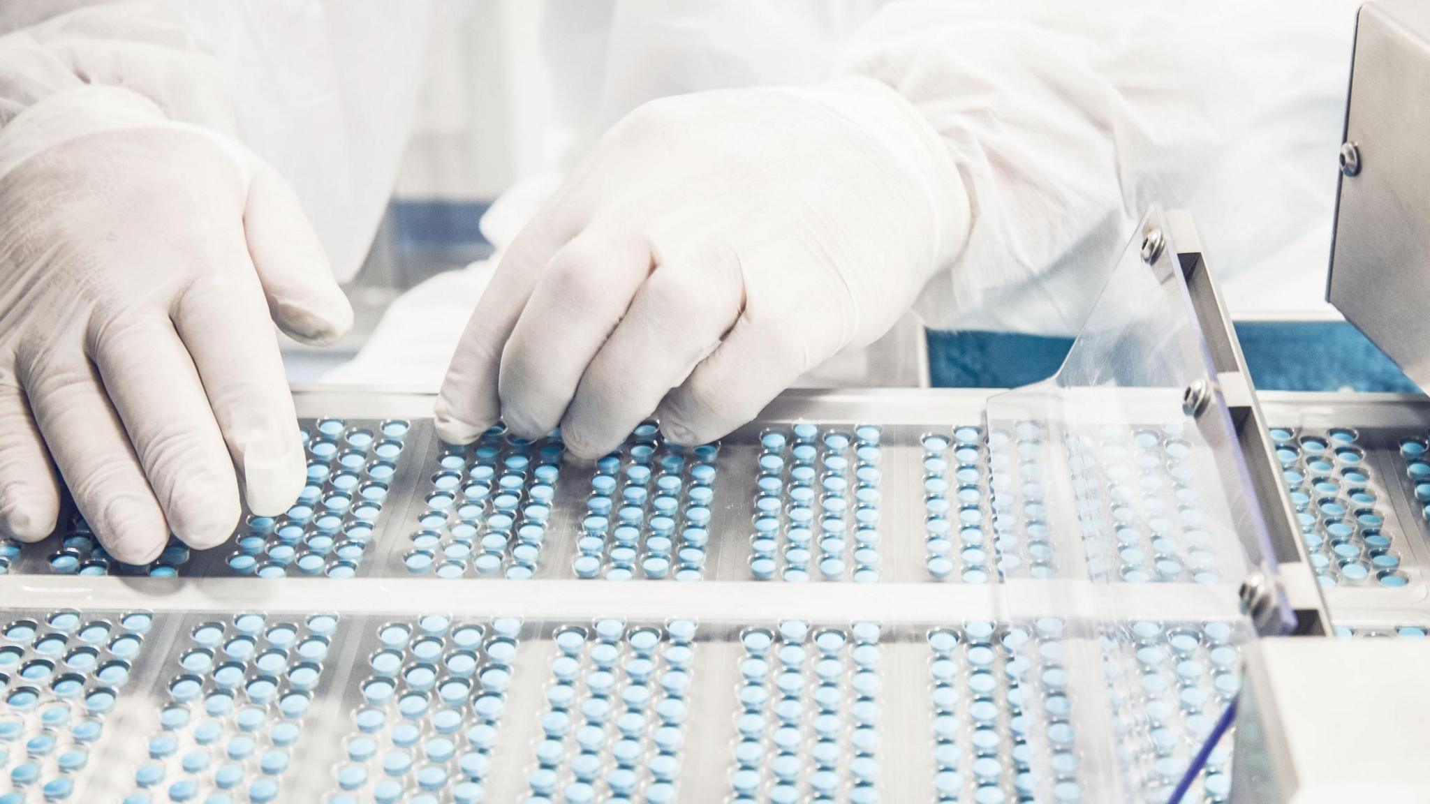 A worker inspects pills on a blisterpack conveyer belt