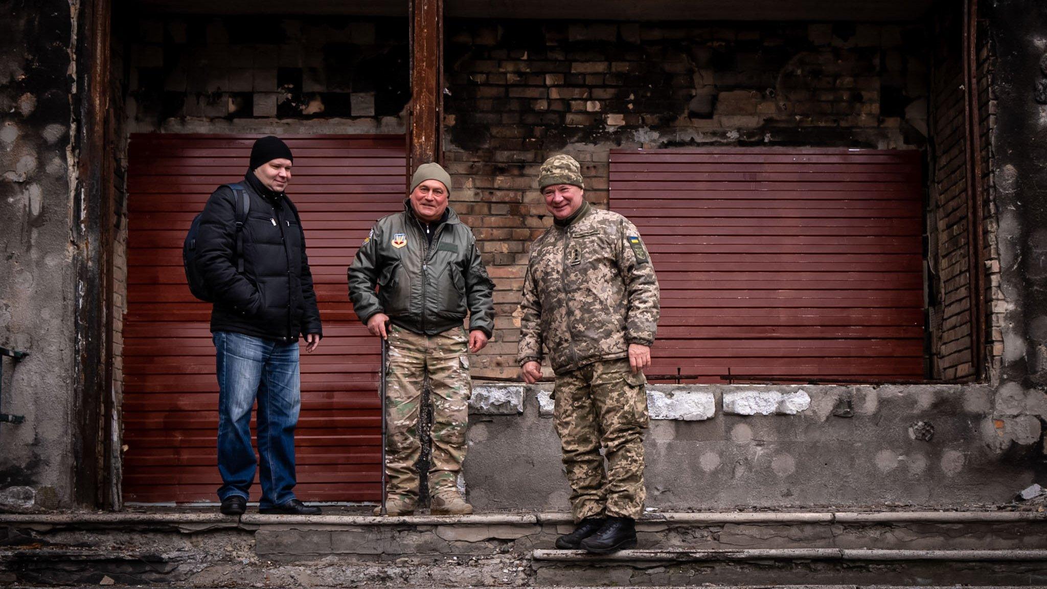 Maksym (L) Volodymyr (C) and 'the colonel' (R) stand in front of their bombed out office for local volunteers