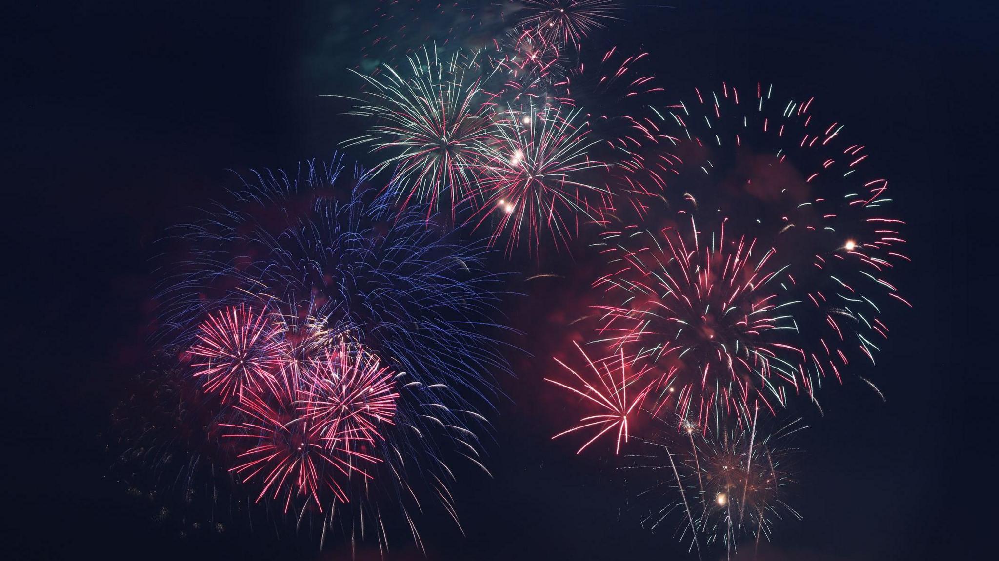 Fireworks exploding in the night sky, they are mostly red but there are also blue and green bursts of light