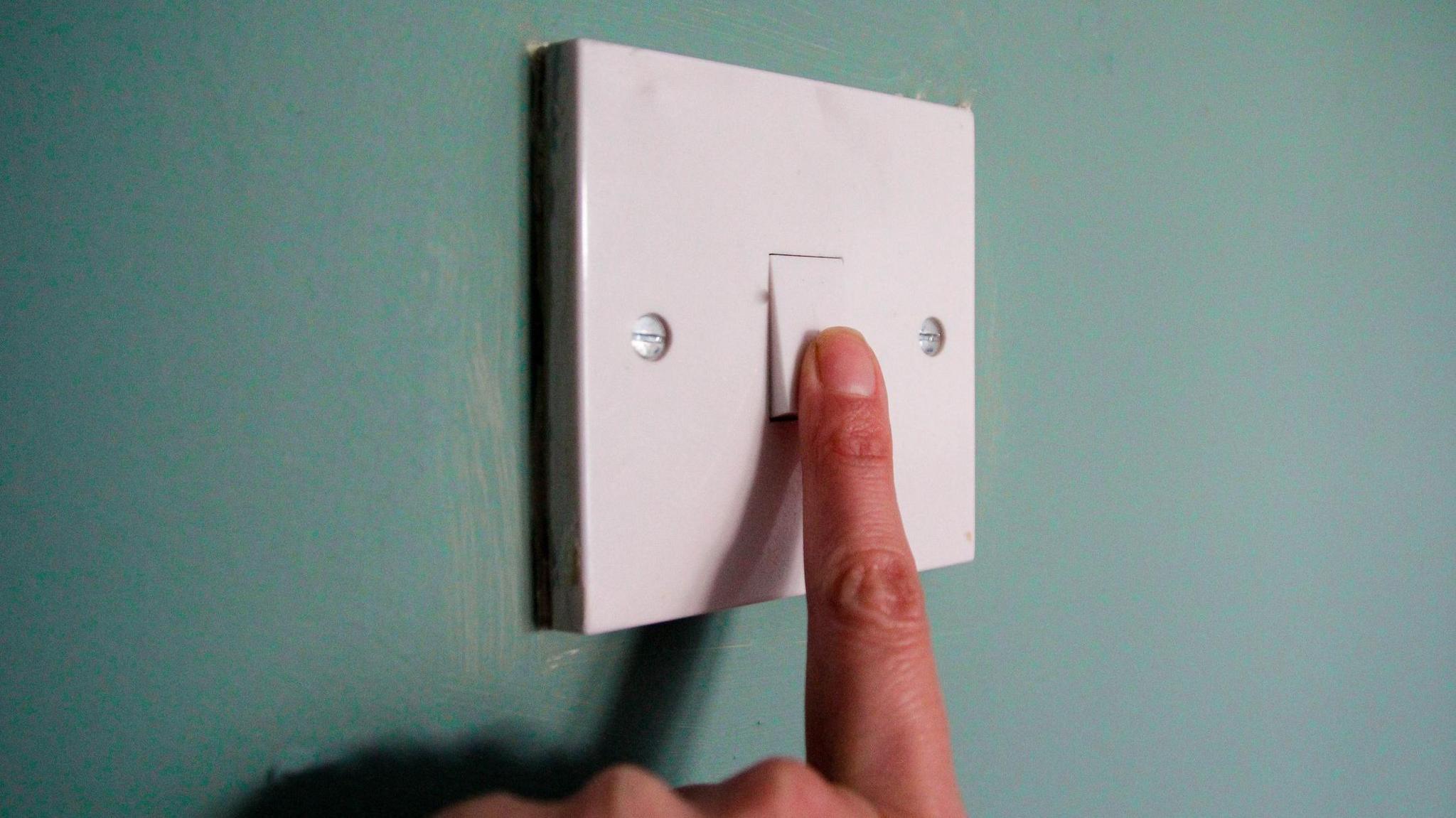 Finger on white lightswitch against green wall 