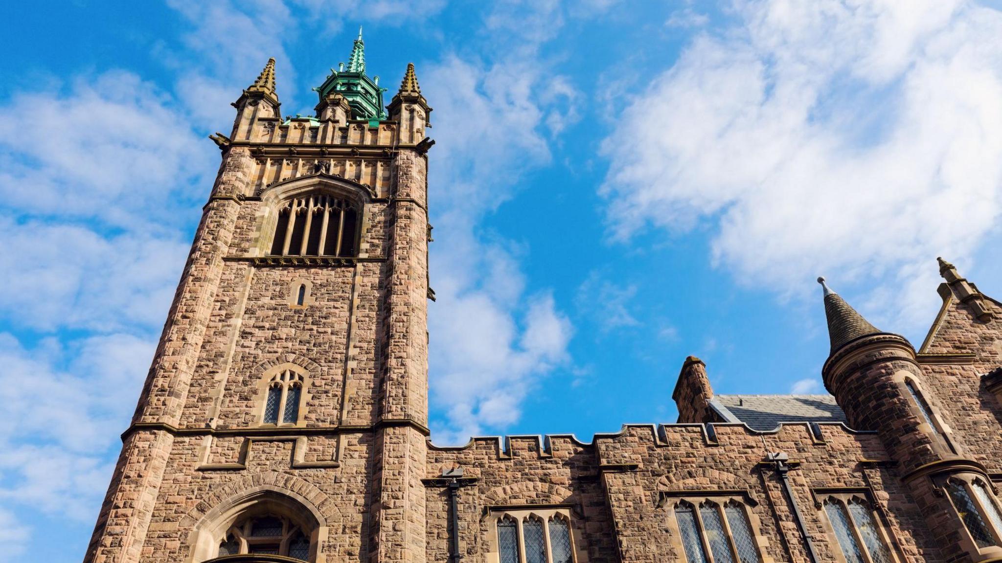 Assembly Buildings in Belfast - an older building with grey brickwork towering in the sky with turrets. The sky is blue with a few clouds above.
