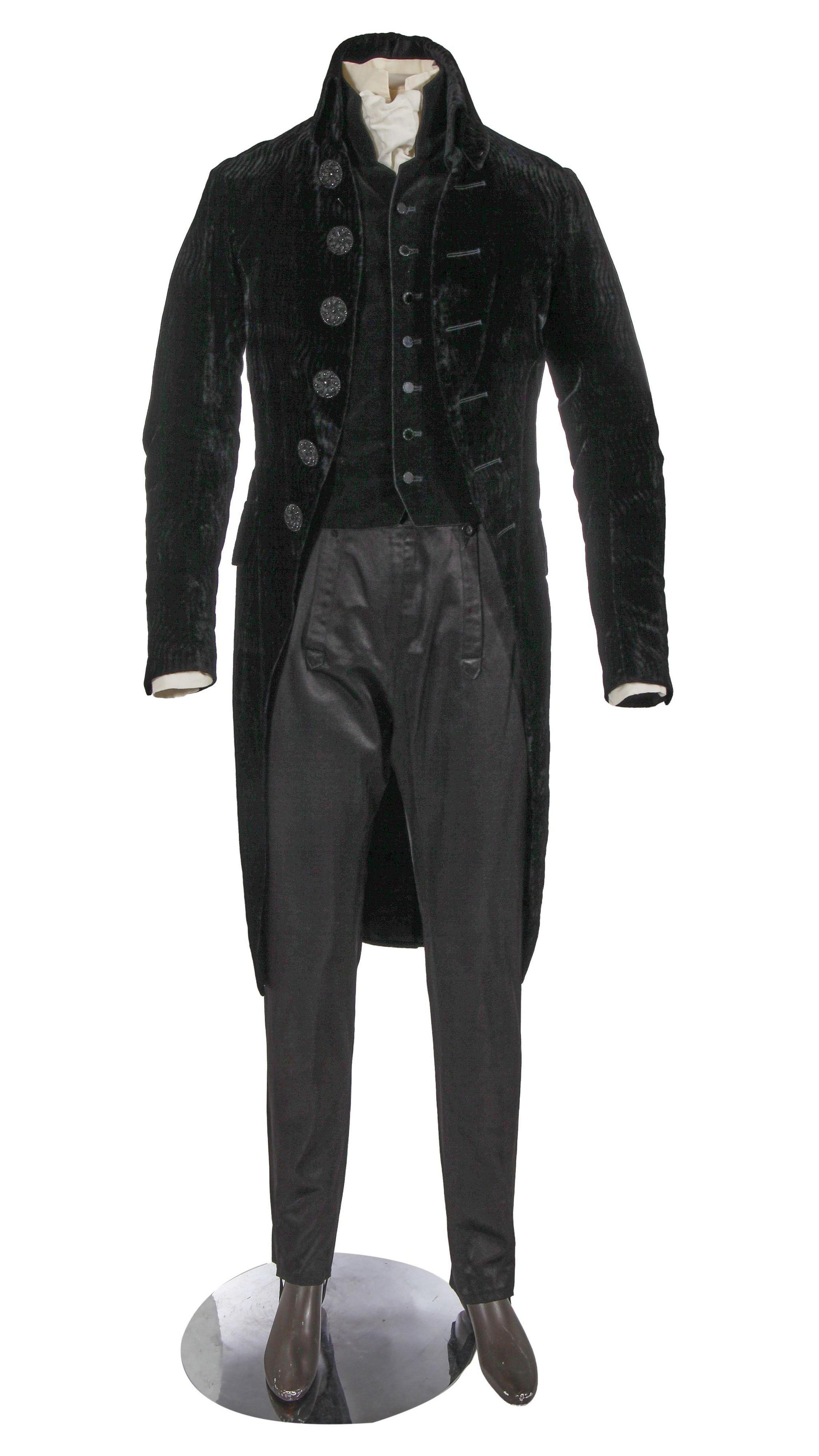 An early 19th century style suit comprising a cutaway black velvet tailcoat, large moulded glass jet-effect buttons, a closely fitting un-patterned black velvet waistcoat, a pair of black satinised wool trousers with elasticated stirrup bands to hems and a cream cotton shirt with matching stock.