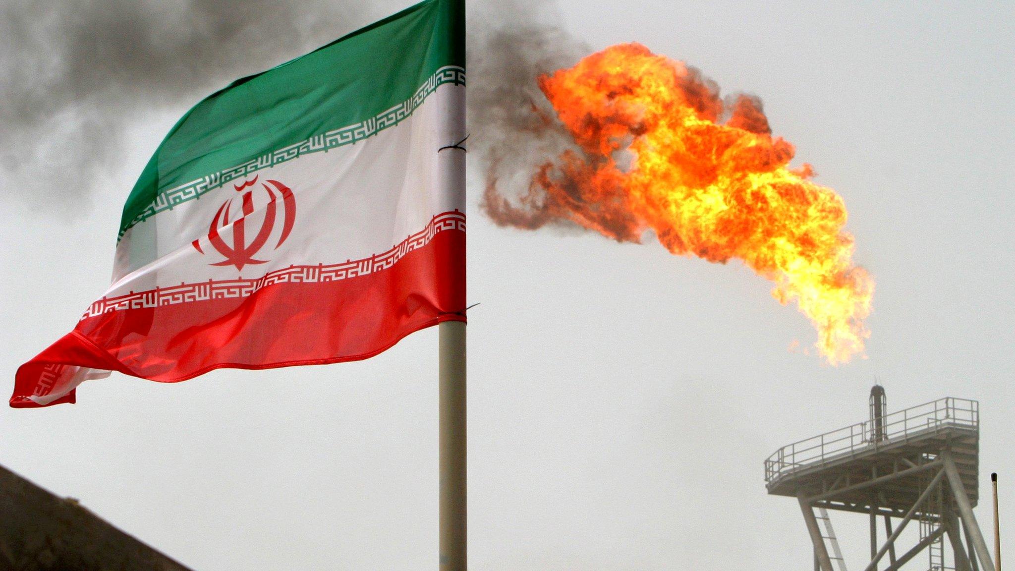 A gas flare on an oil production platform in the Soroush oil fields is seen alongside an Iranian flag in the Persian Gulf, Iran