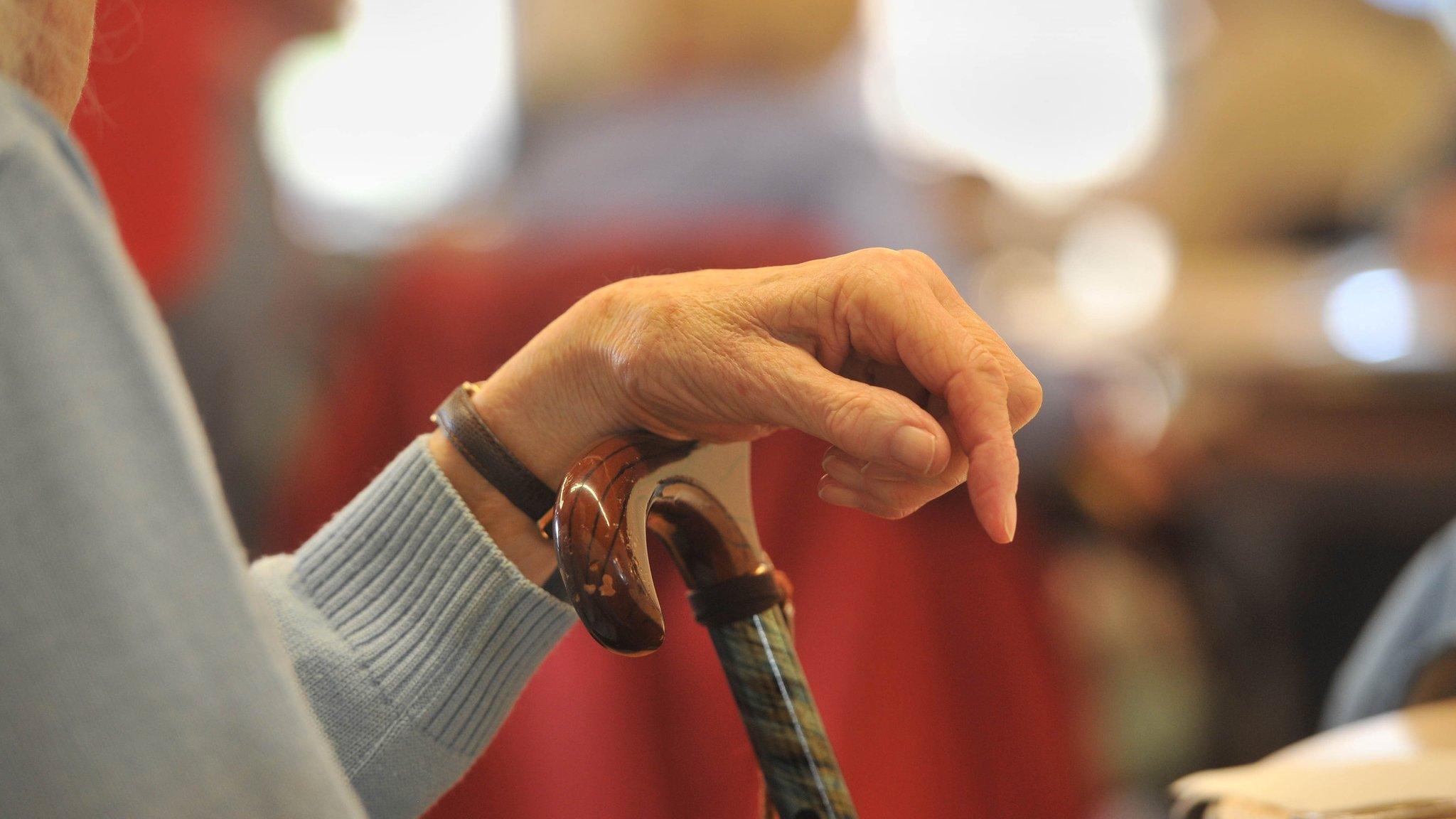 An elderly woman's hand on a walking stick