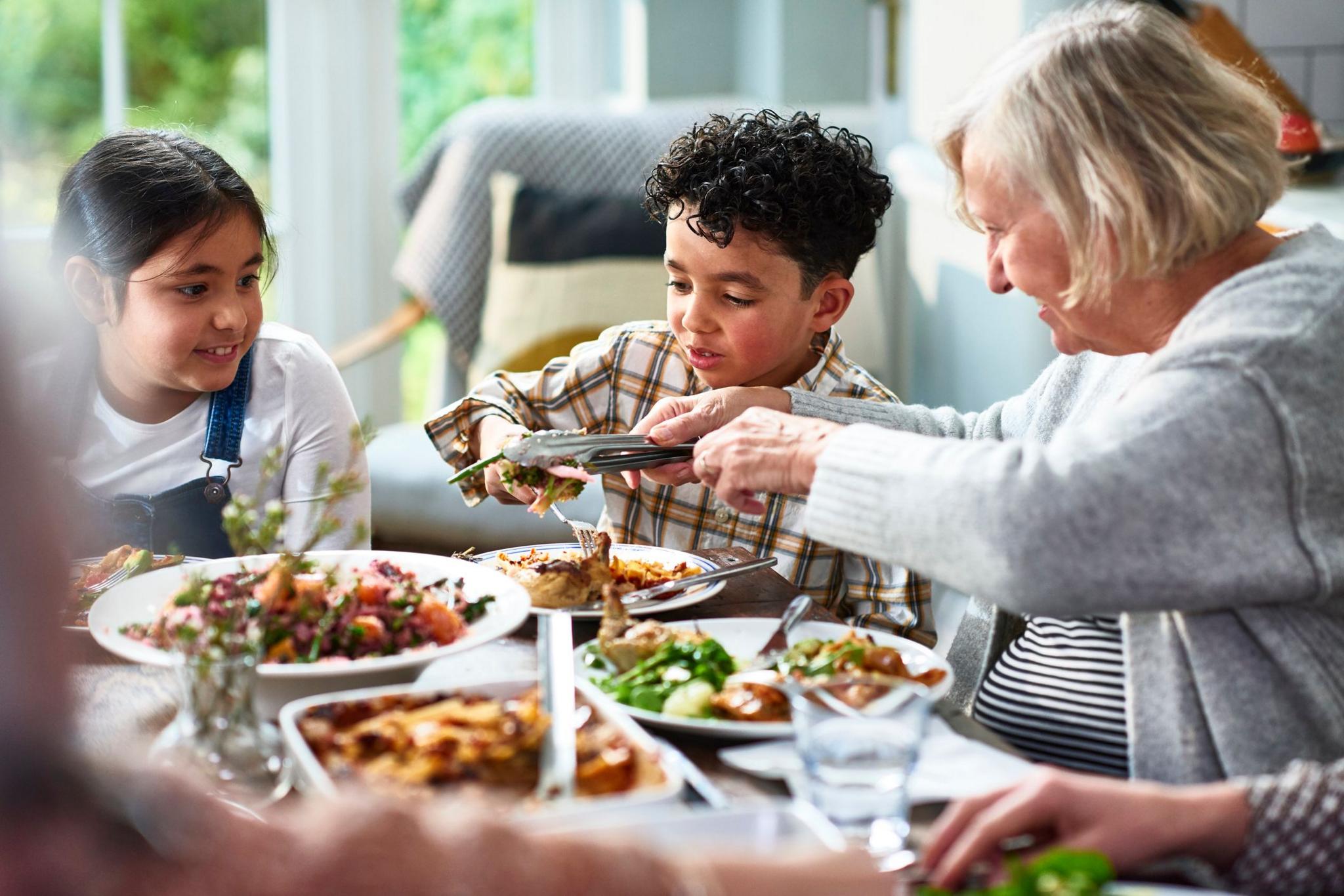 Grandmother and children with group of relatives sitting at dining table enjoying home-cooked meal