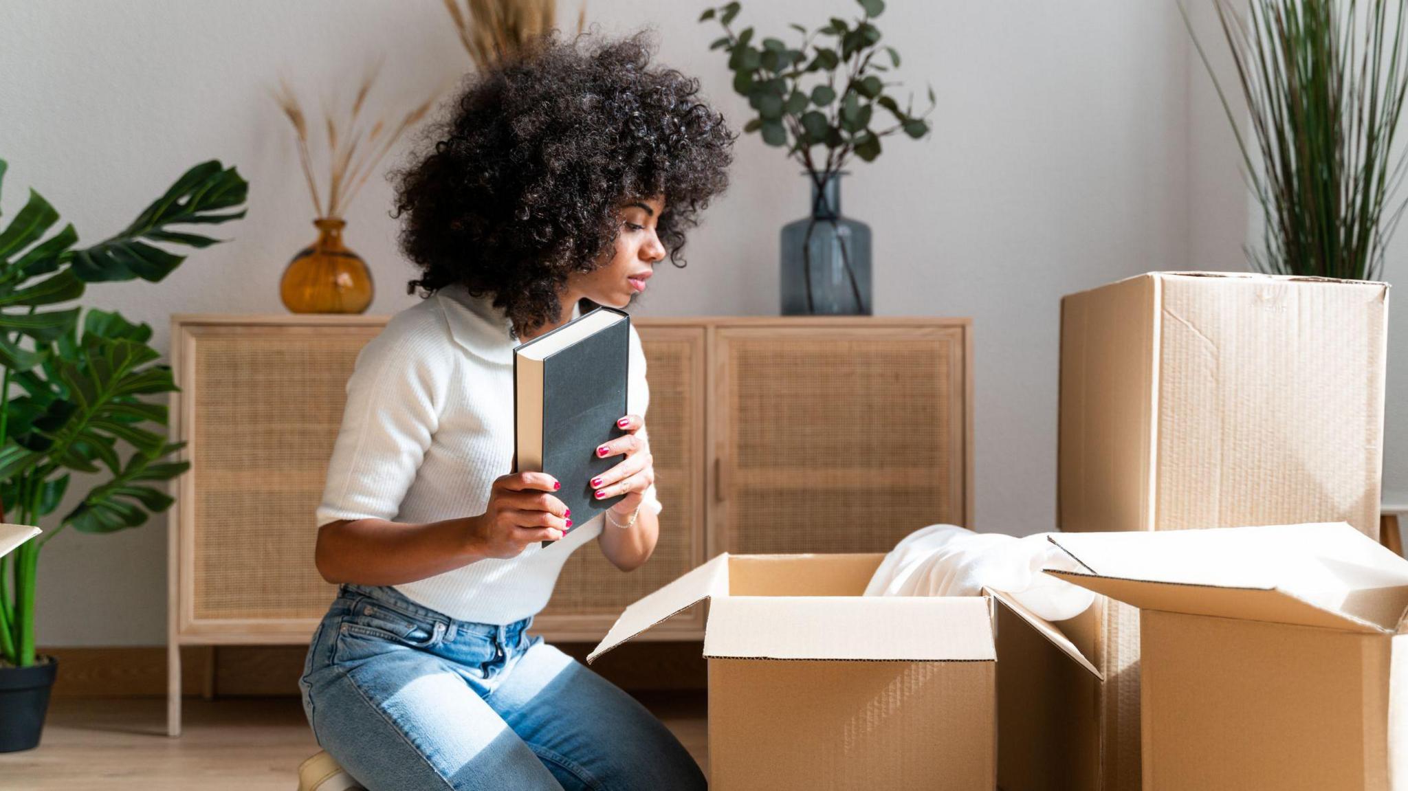 Woman unpacks boxes in a new home with a book in her hand.