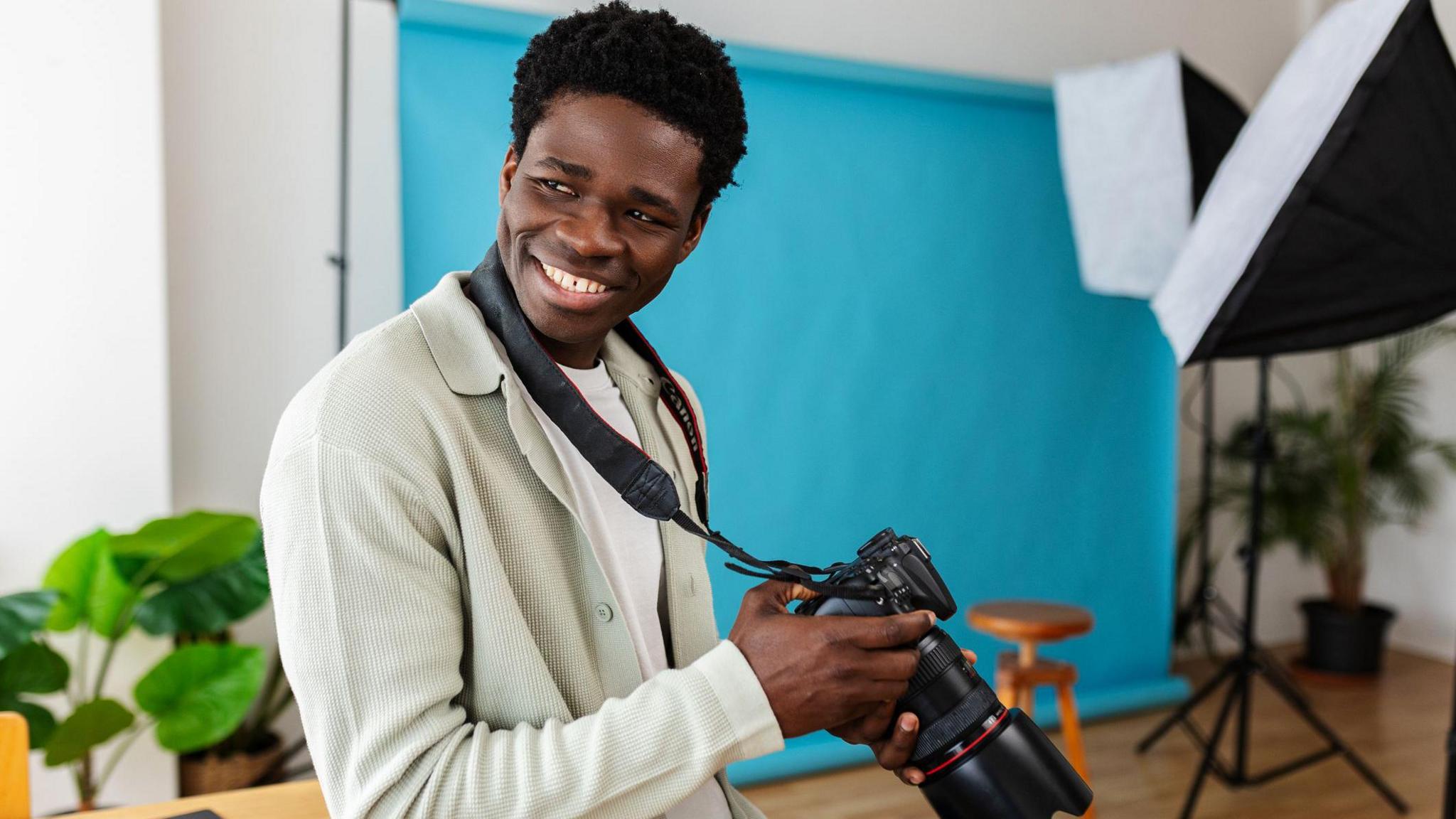 A young man holds his camera and smiles to someone out of shot.