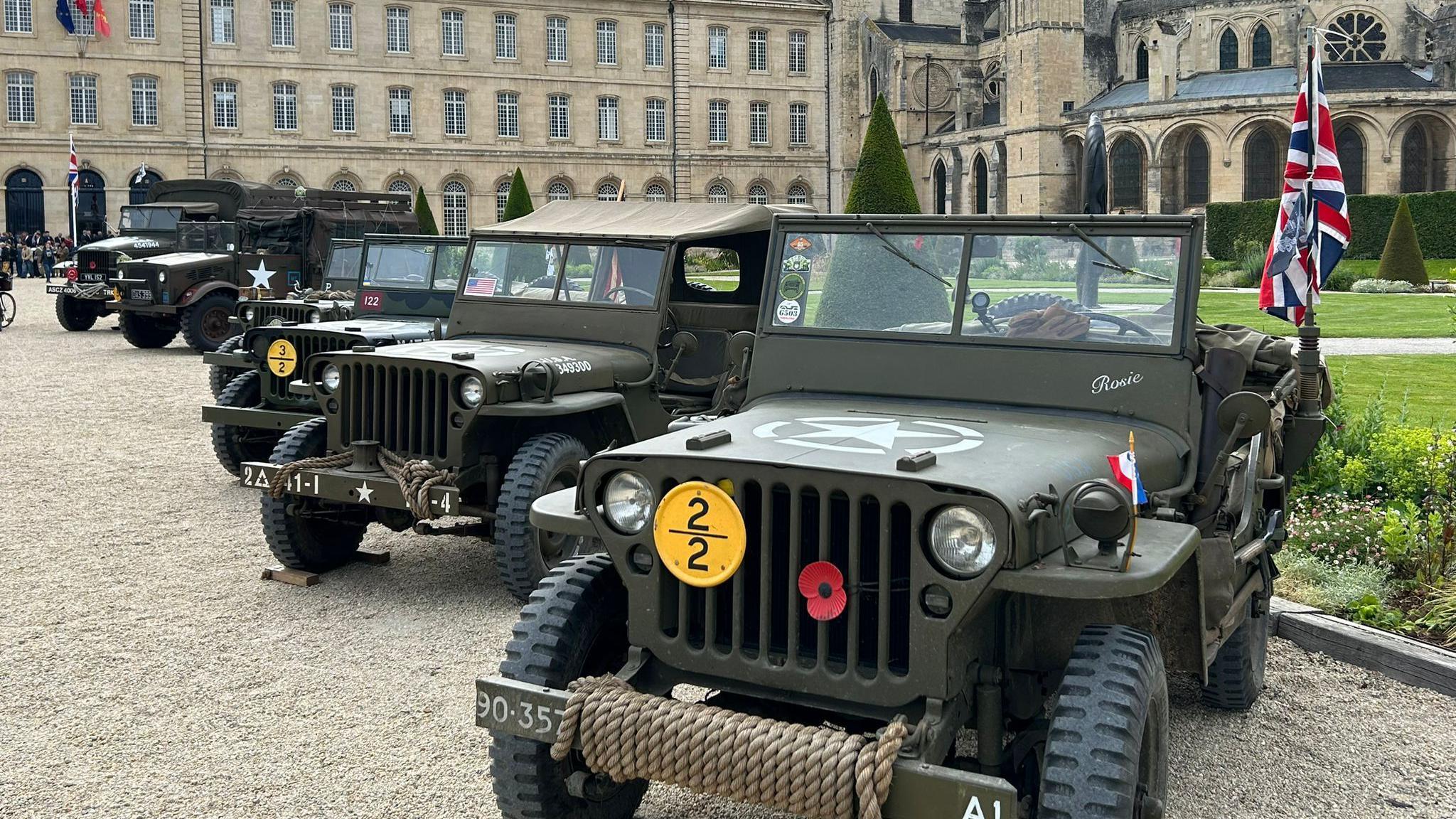 A line of old military jeeps in front of a grand French building