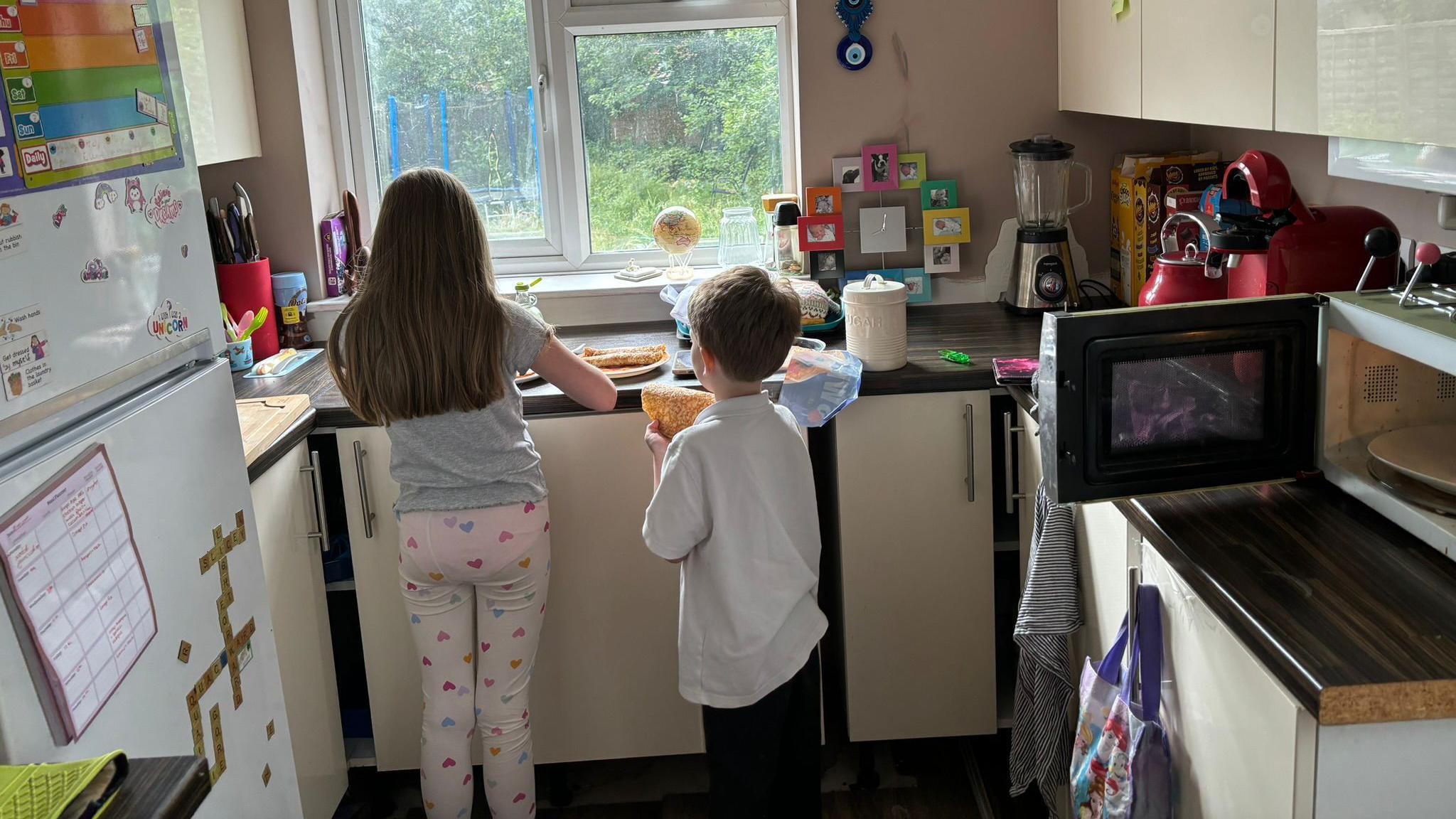 Two children facing away from the camera making breakfast in a kitchen