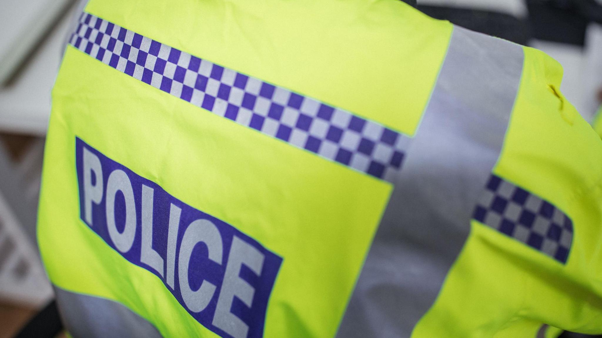 Stock photo showing the back of a police officers yellow high vis jacket. 