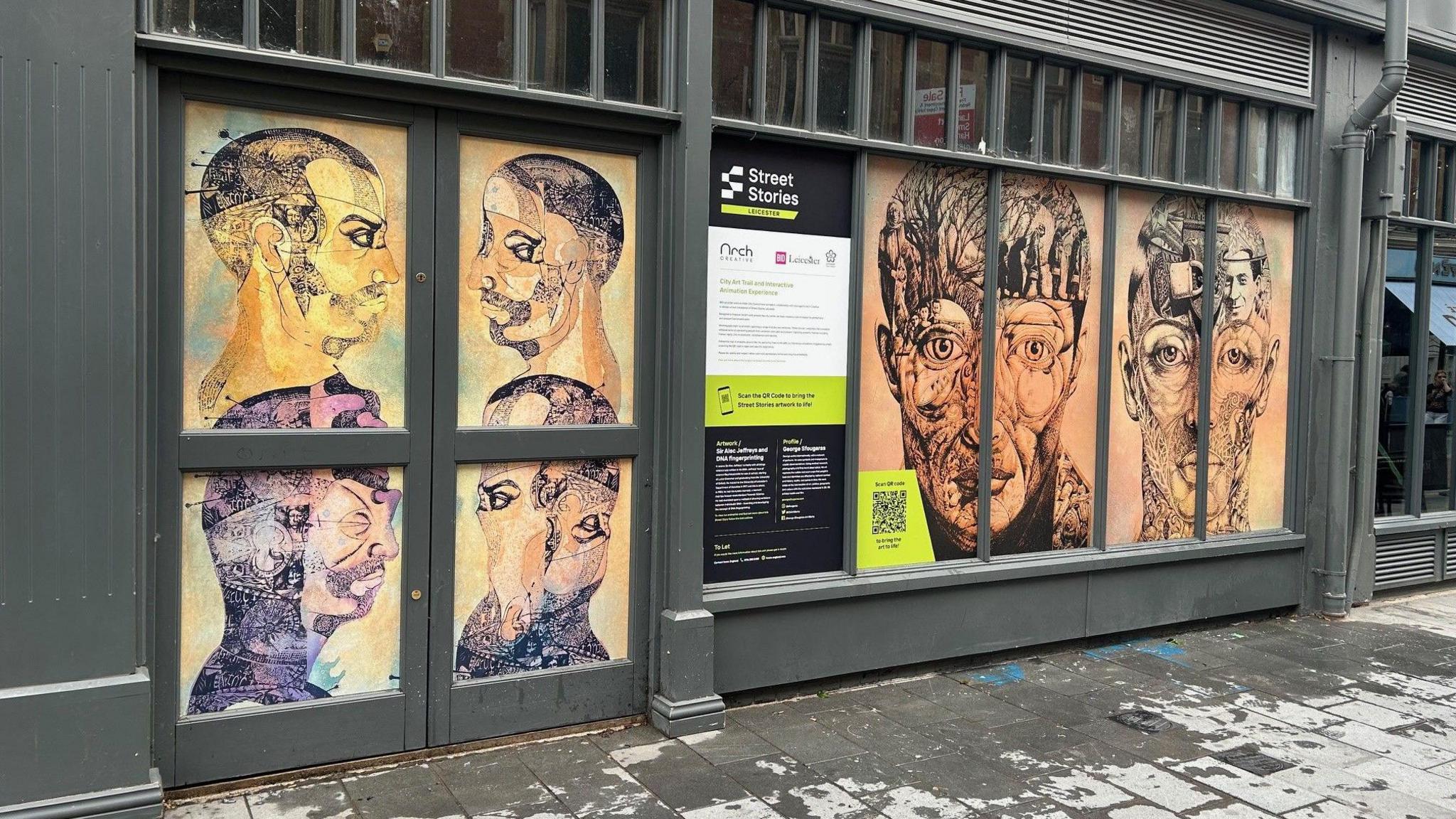 A dark-framed shop front with abstract art of human heads and profiles in the window.