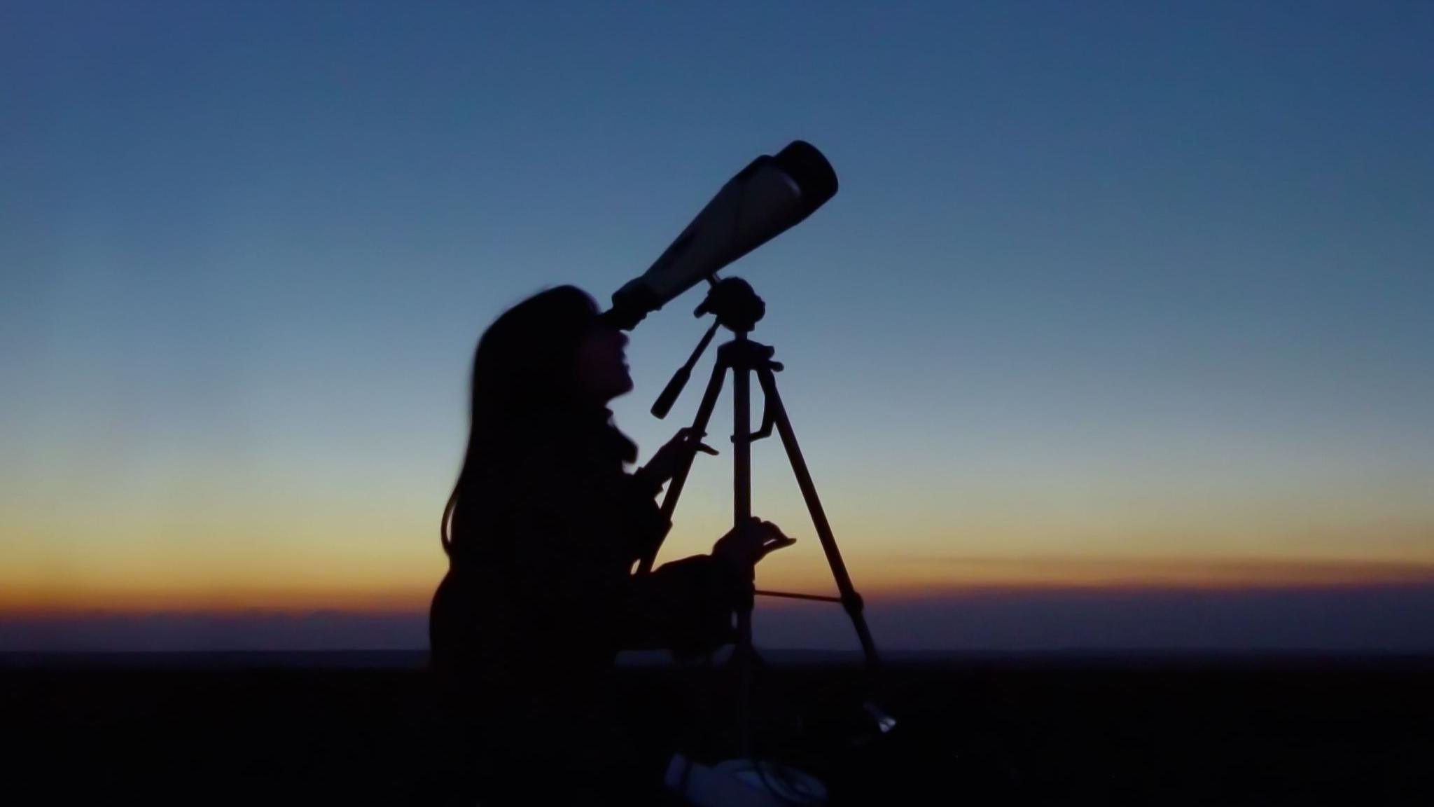 Woman looks up at night sky using a telescope