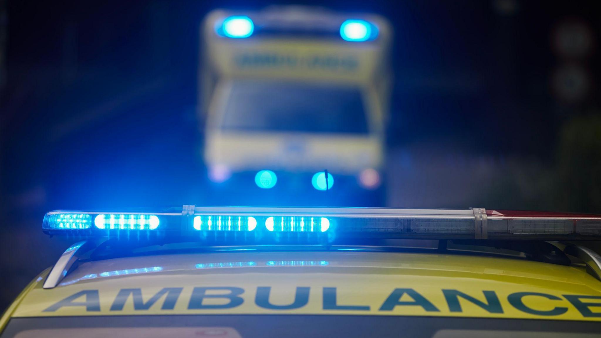 A stock image of an ambulance's blue lights flashing, with another ambulance in soft focus behind them.