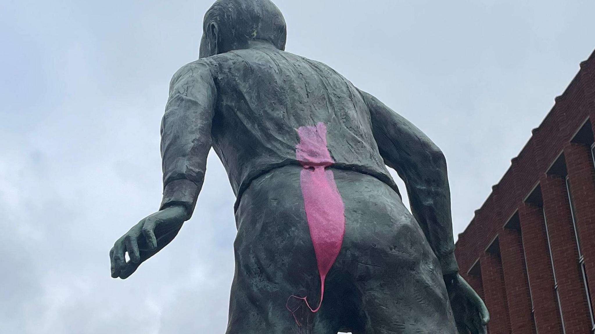 The rear of a grey statue of a footballer with a thick pink coloured substance sprayed down its back