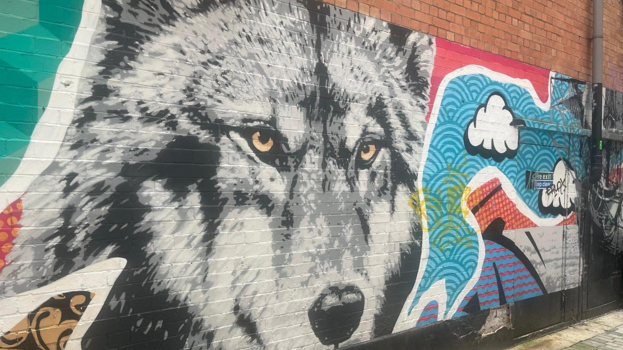 Artwork on a wall that shows a wolf surrounded by abstract shapes coloured blues red green yellow and white