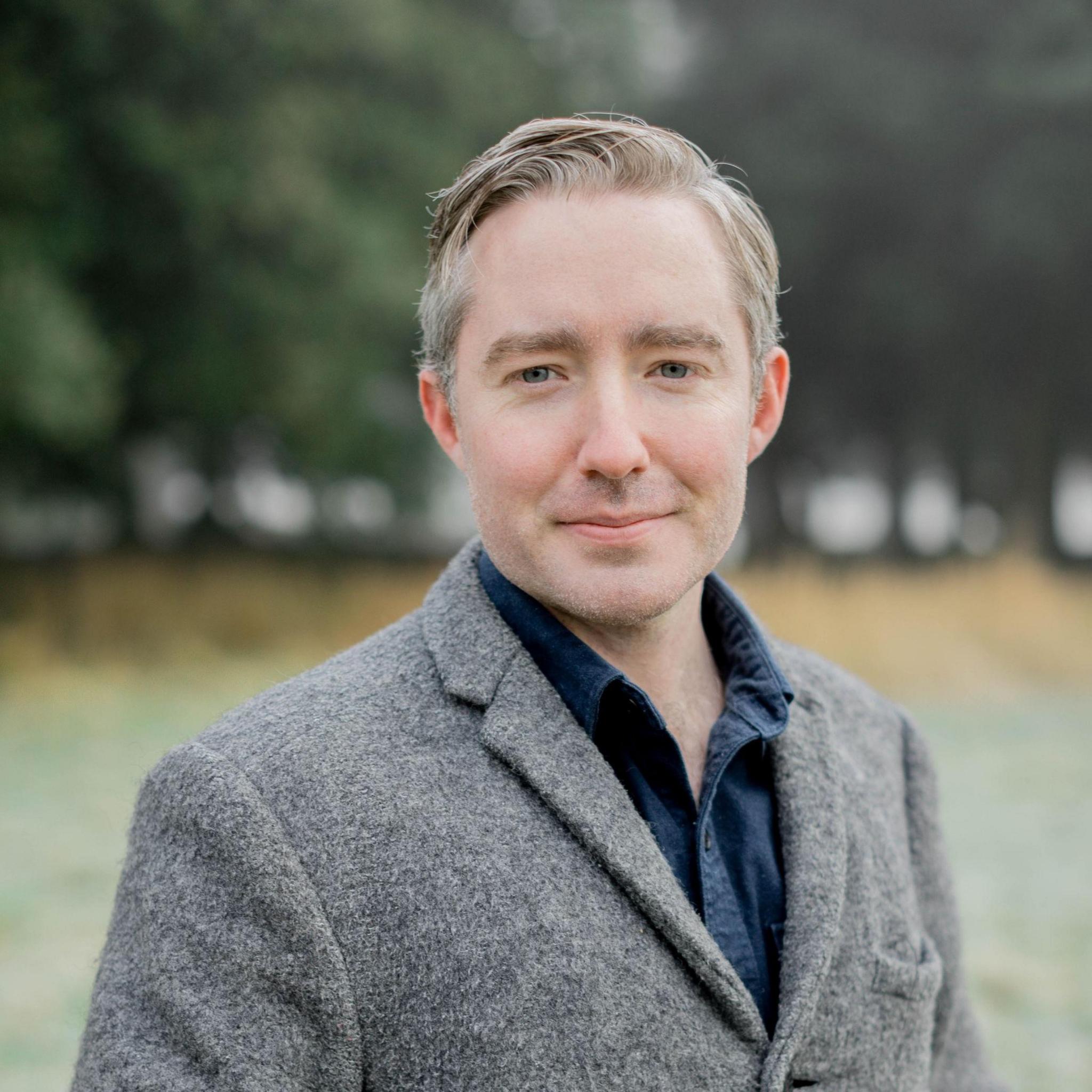 Lonán Ó Briain standing outside wearing a grey jacket and blue shirt