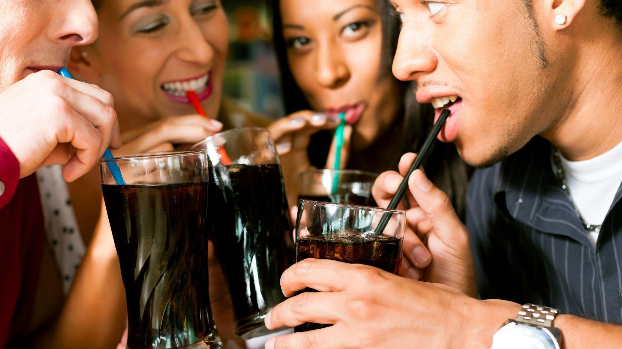 Four friends drinking soda in a bar with colorful straws