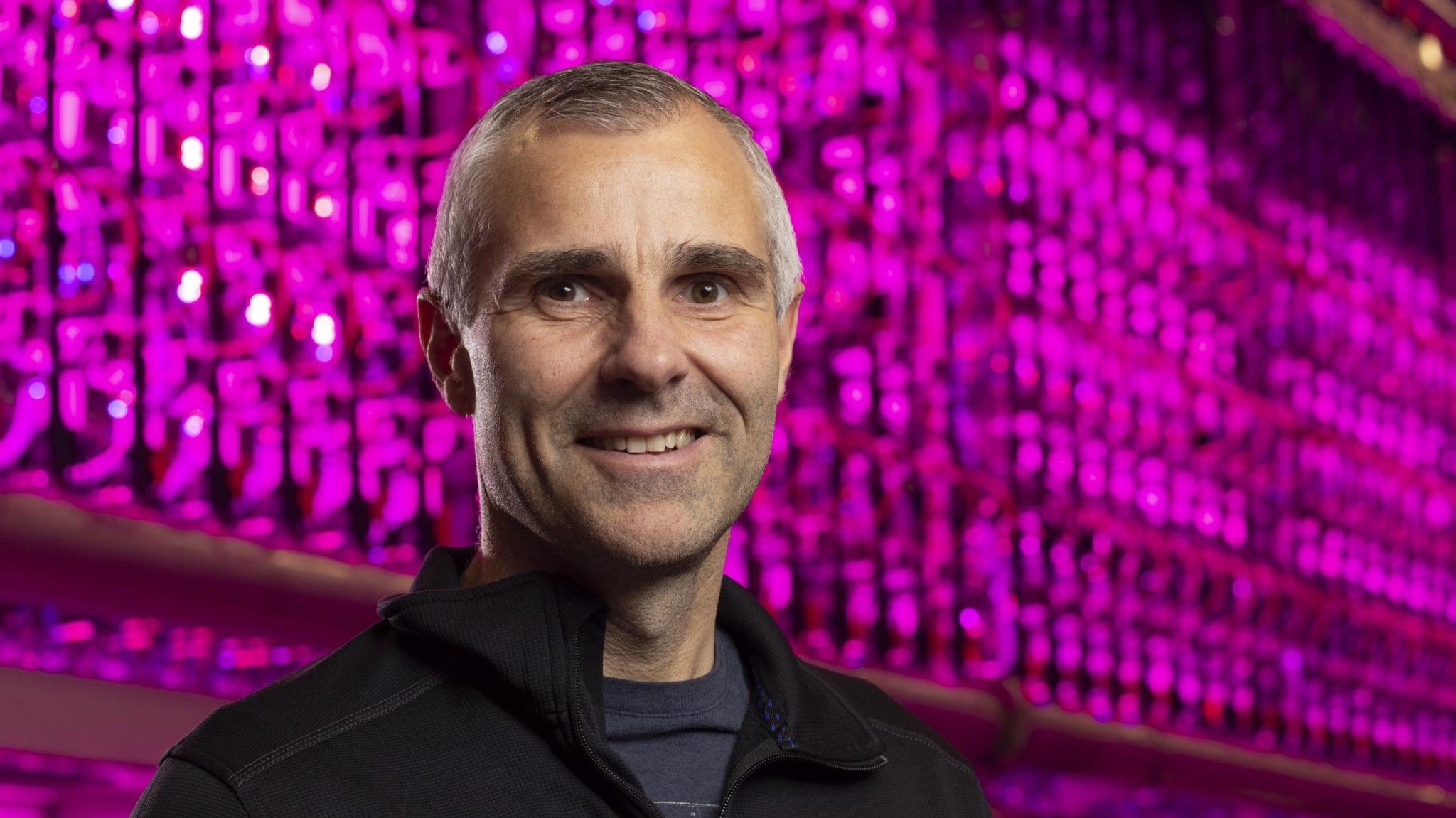 General Manager, Kristinn Haflidason standing in front of bioreactors giving off a pink-purple light