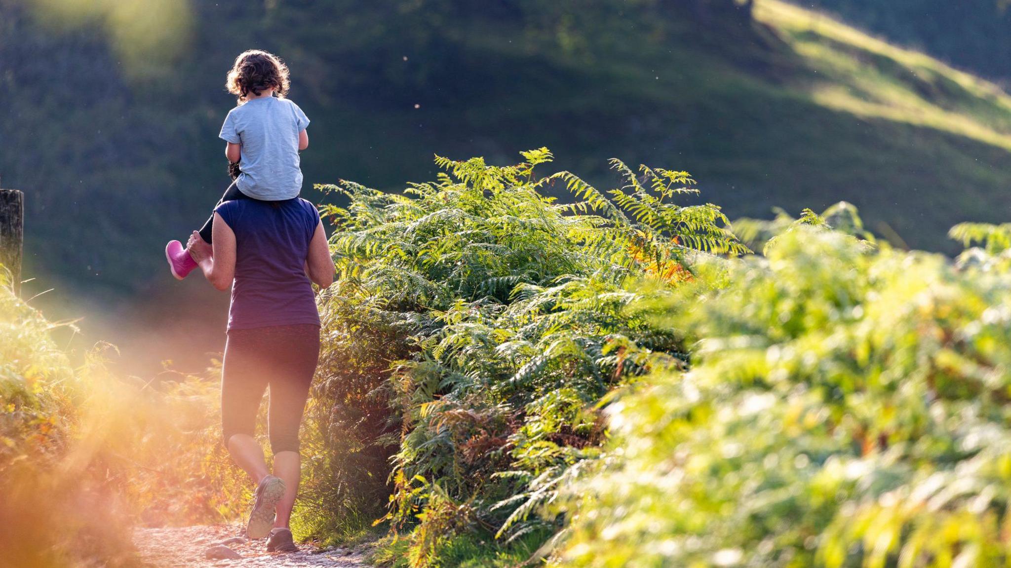 Woman carriers child along a path in the countryside, in sunny weather