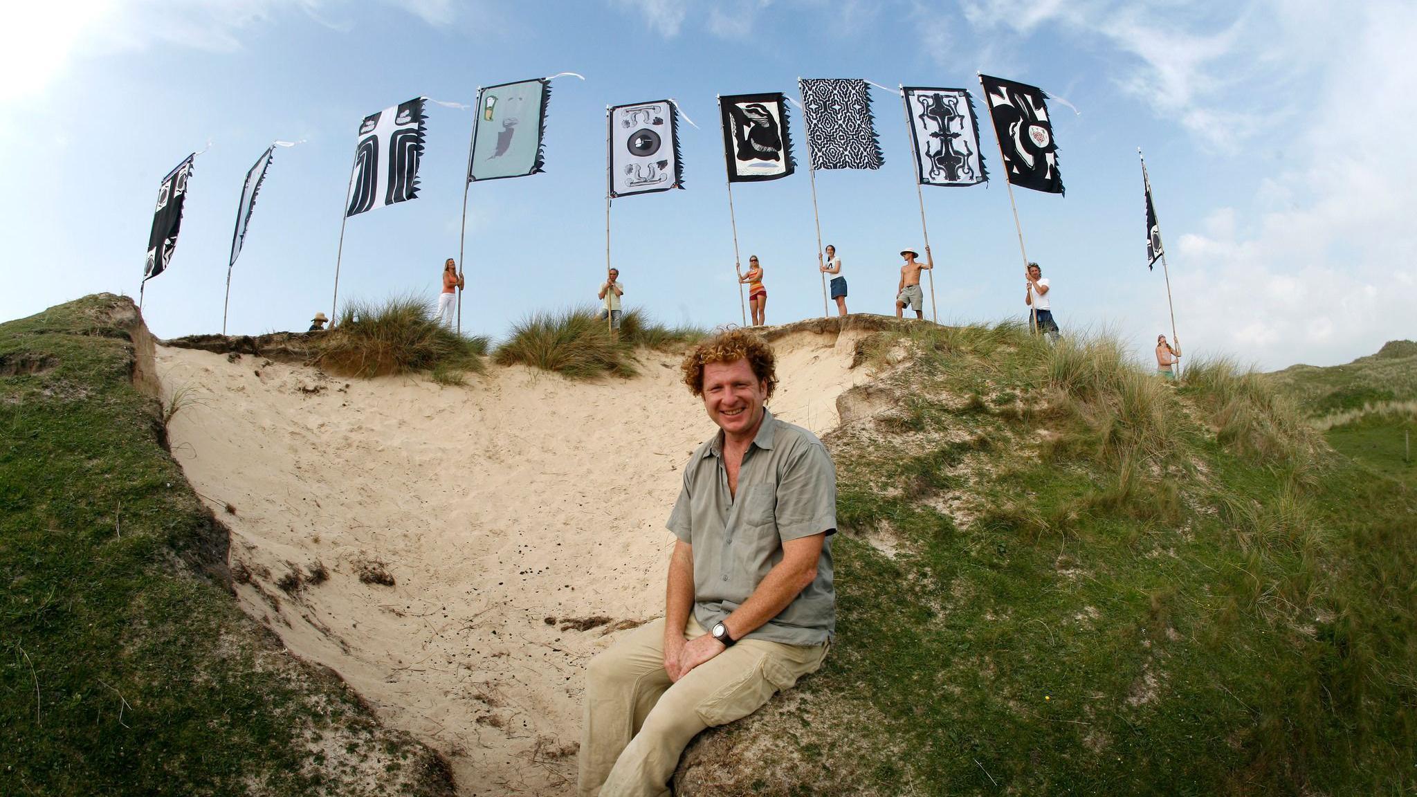 Angus Watt sitting in front of a row of WOMAD flags