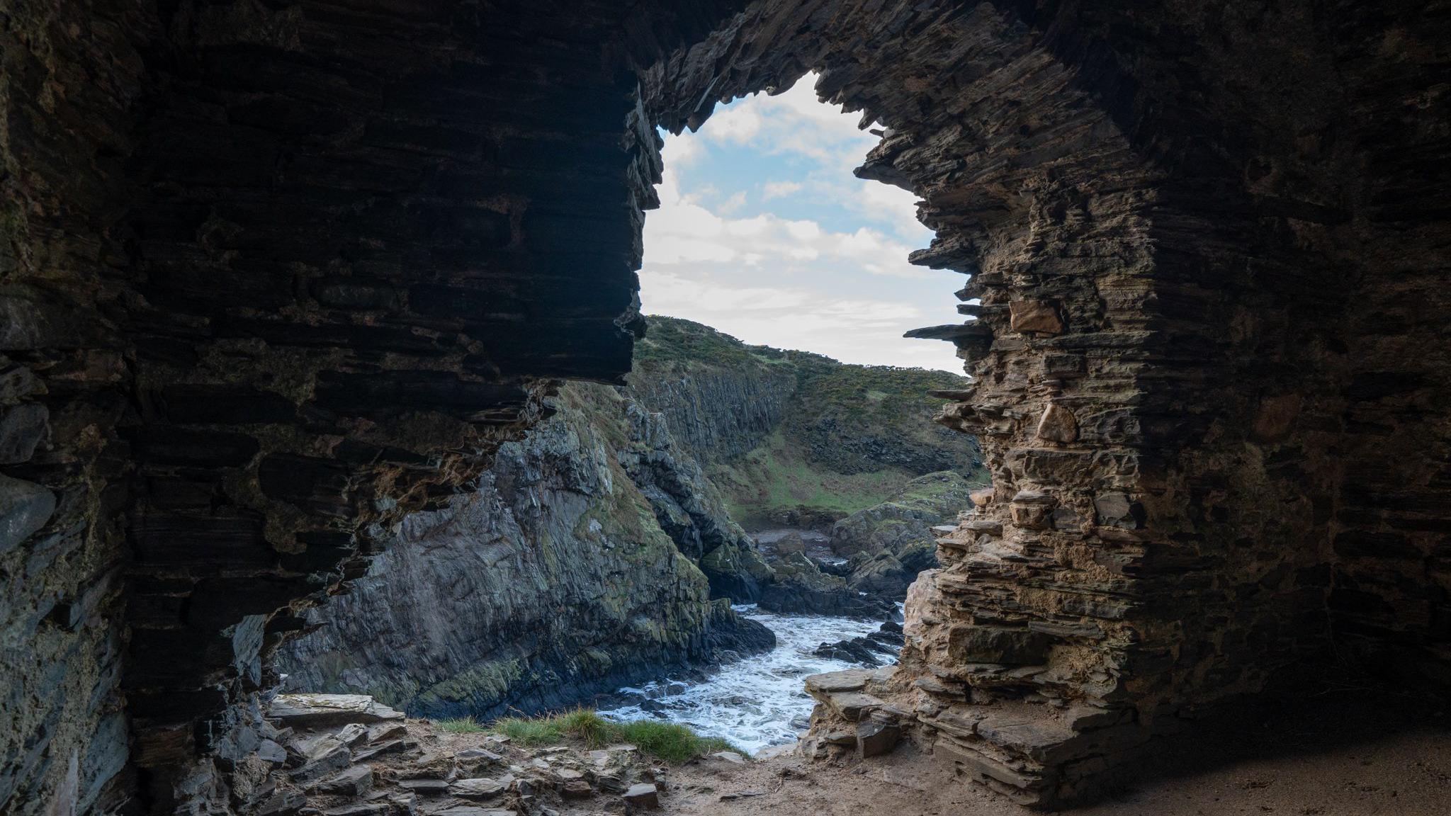 A photo taken through a gap in the rocks looking onto more cliffs and the water