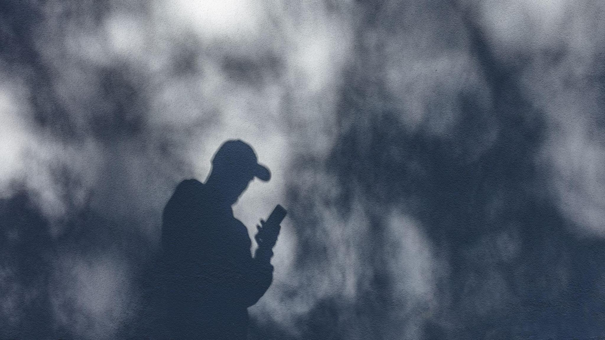 Shadow of a an watching his phone against a plain wall. 