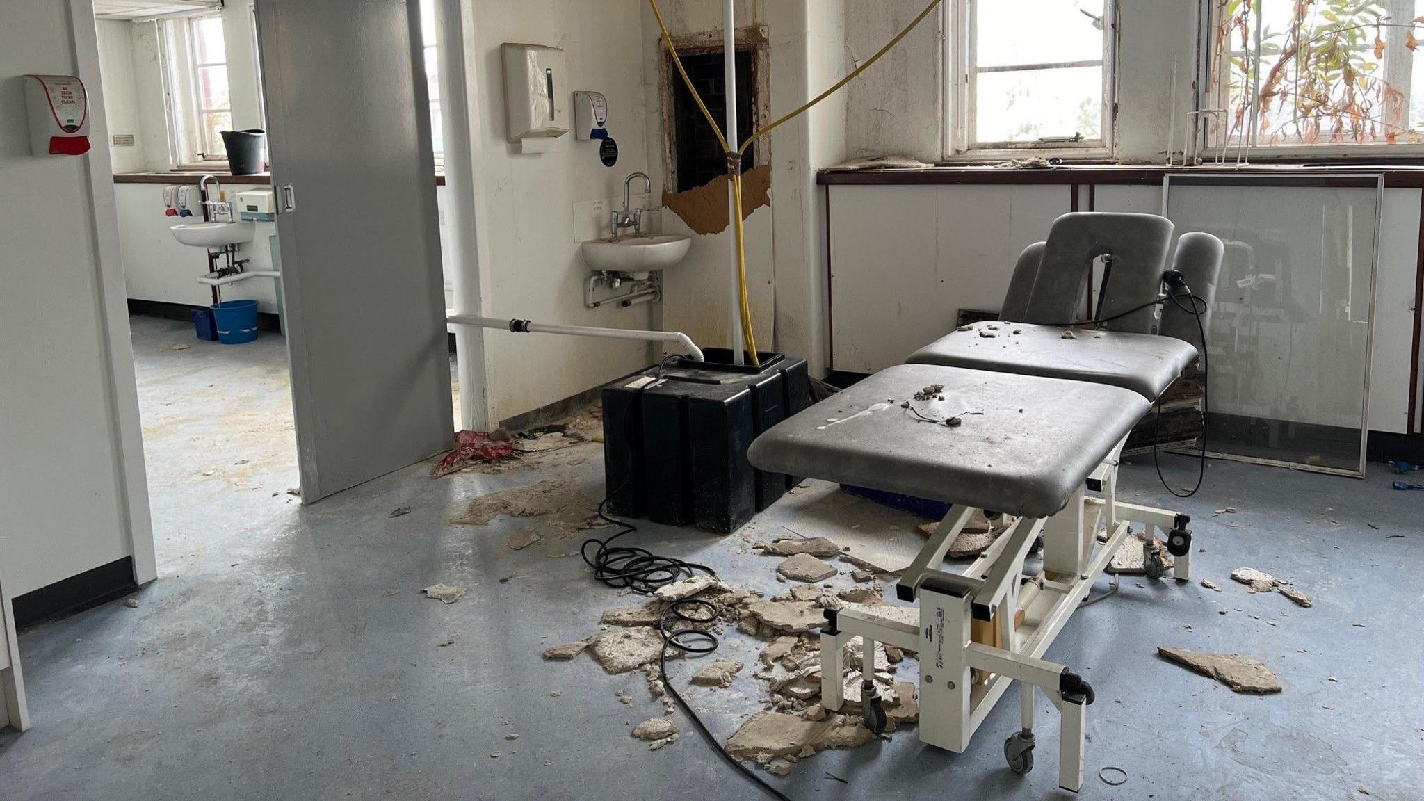 A hospital bed in the middle of a room surrounded by crumbling plaster