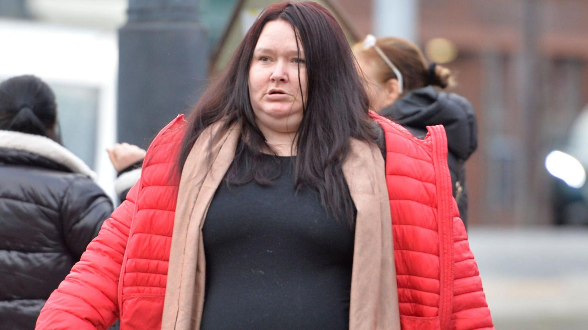 Elaine Lannery photographed outside the High Court in Glasgow. She has long dark brown hair with a middle parting. She is wearing a black top, beige cardigan and a red down jacket. Lannery is not looking at the camera and her mouth is slightly open. 