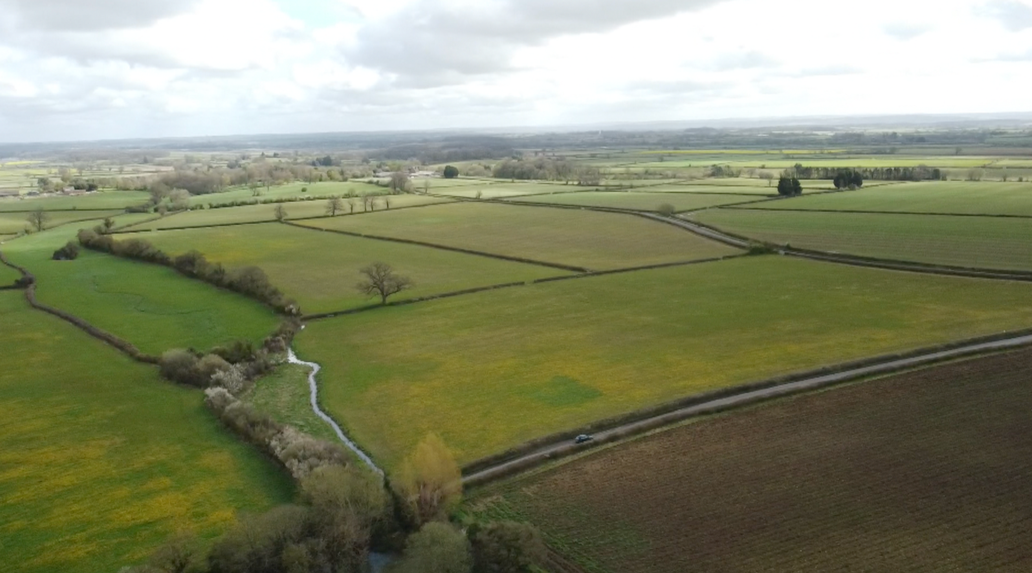 An aerial view of the farmland where the solar panels might be built. They are big, green fields with bush hedgerows.