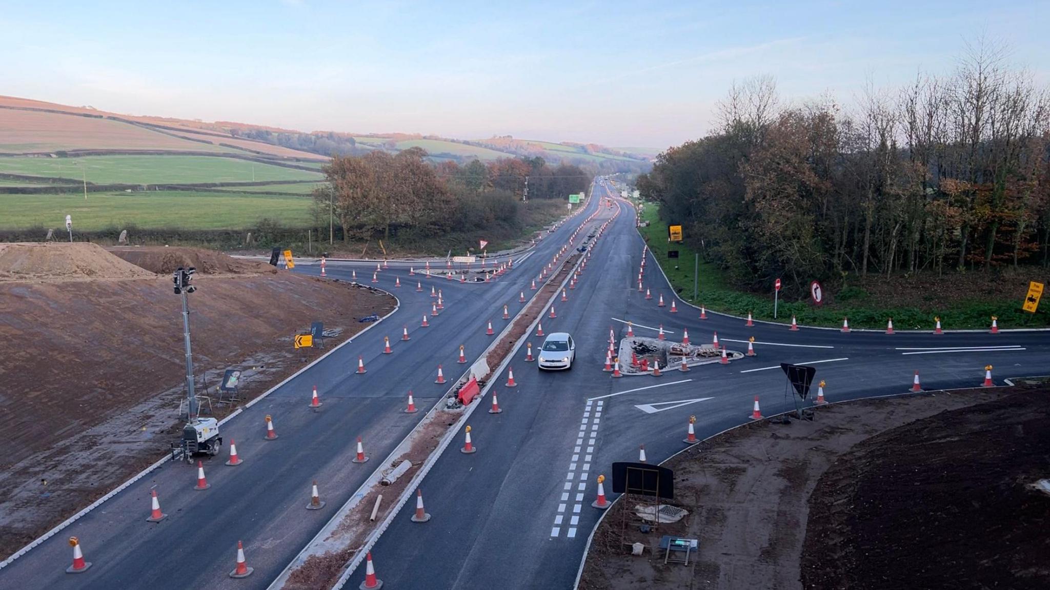 A view from the bridge of the North Devon Link Road with traffic cones lining the unmarked road and a car driving towards the camera