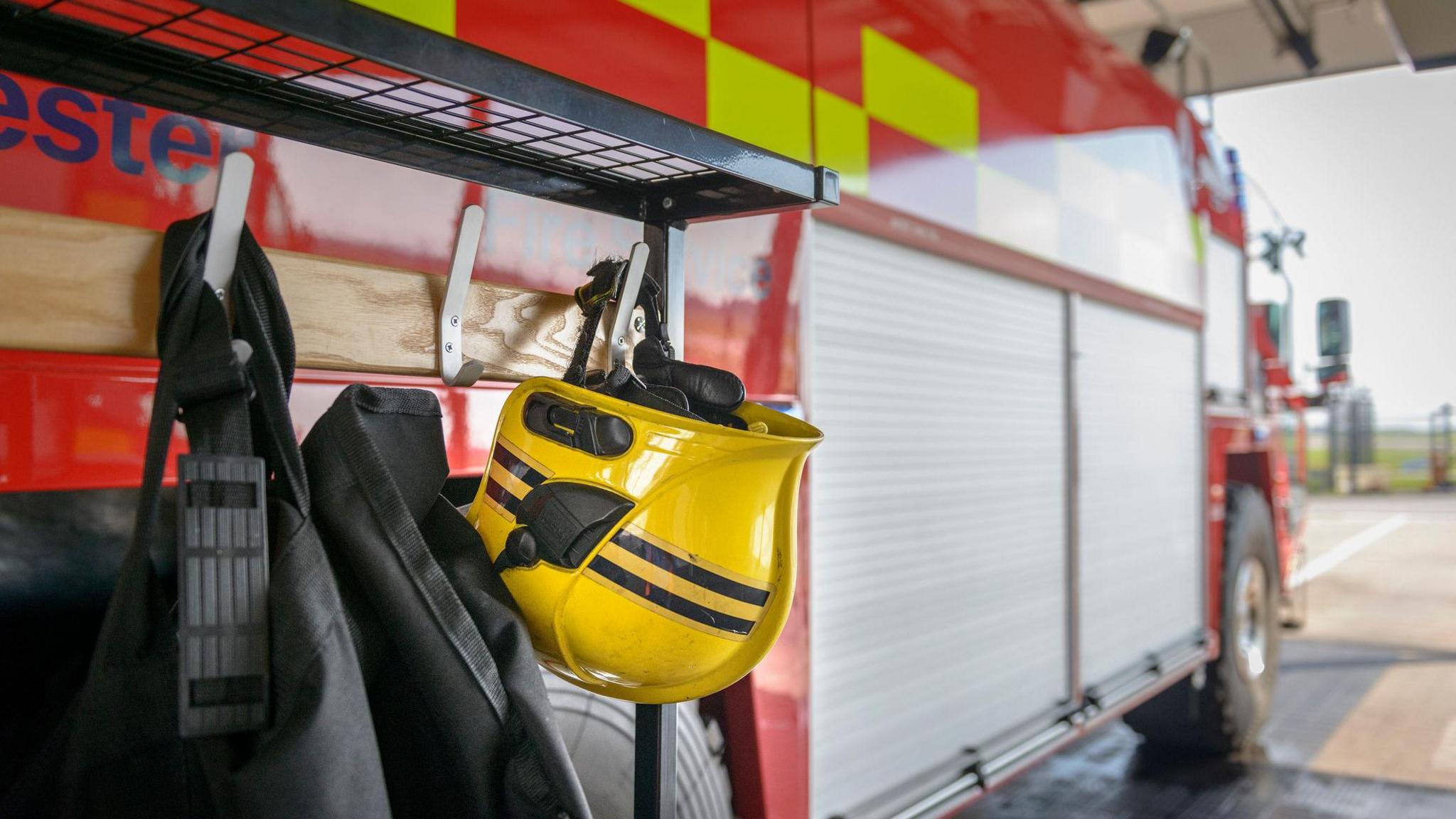 A stock photo of a yellow firefighter's helmet hanging from a fire engine