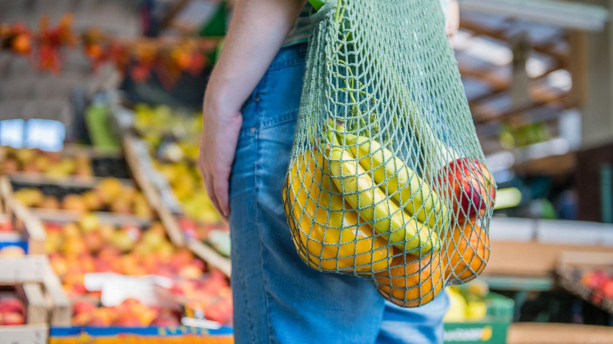 A string bag full of fruit and vegetables and with a market stall visible in the background