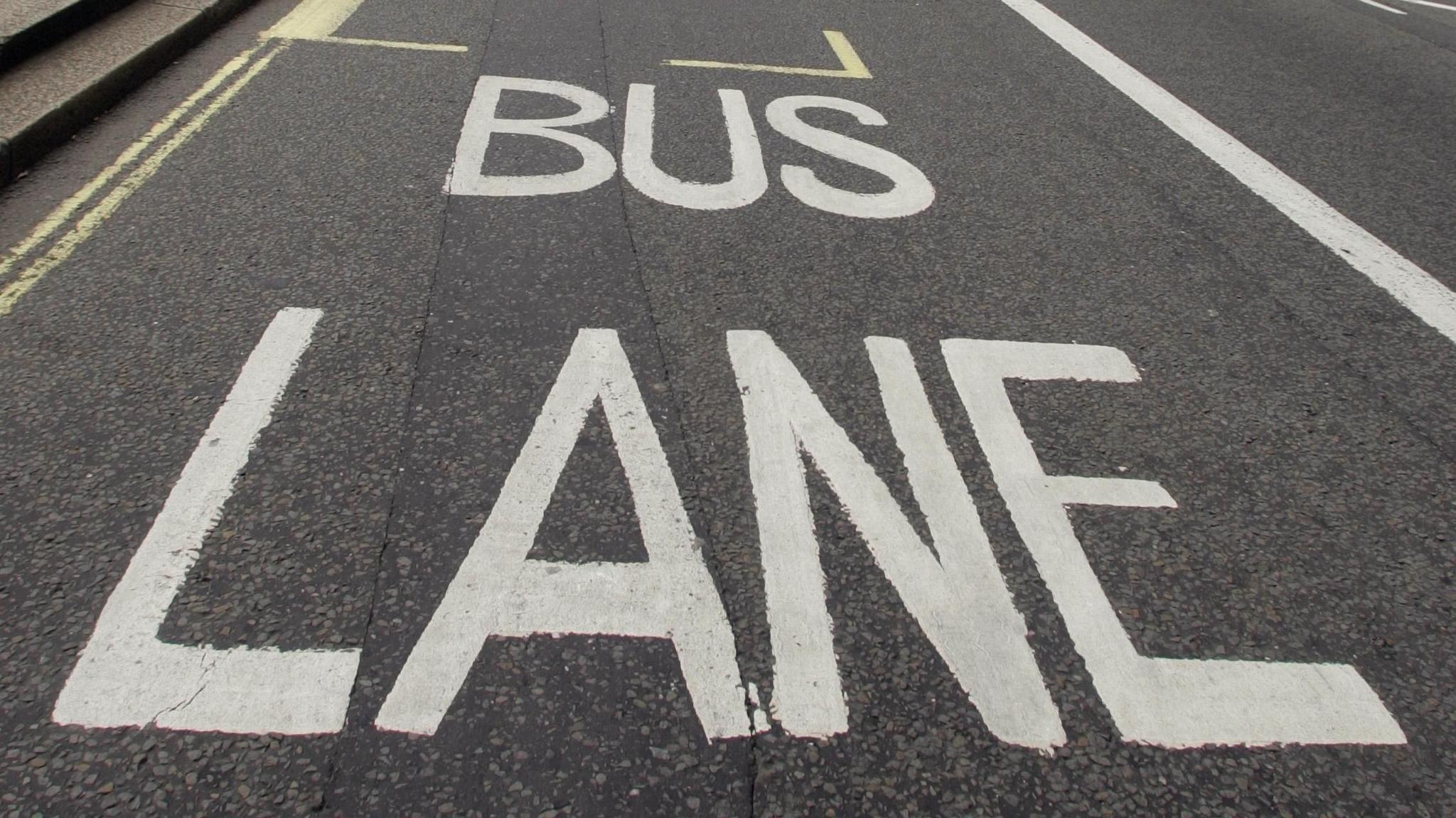 A bus lane sign painted in white on a tarmac road