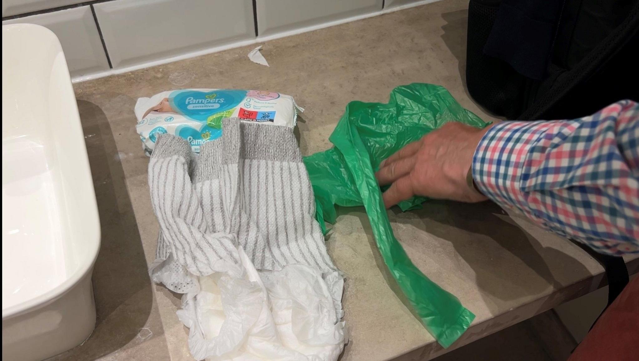 An adult nappy, nappy bag and wipes lie on a bathroom unit