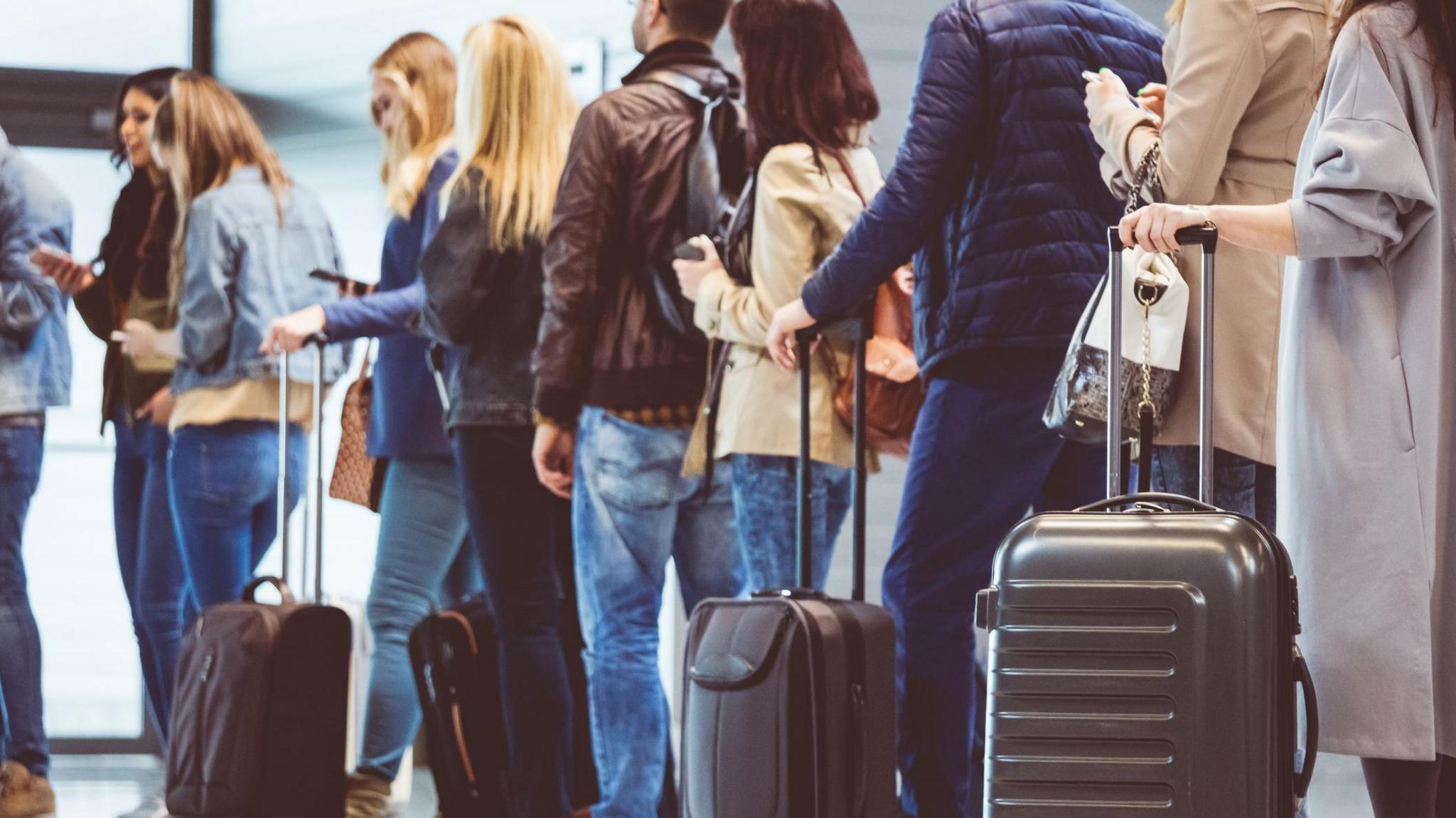 People queuing in airport with wheelie bags next to them
