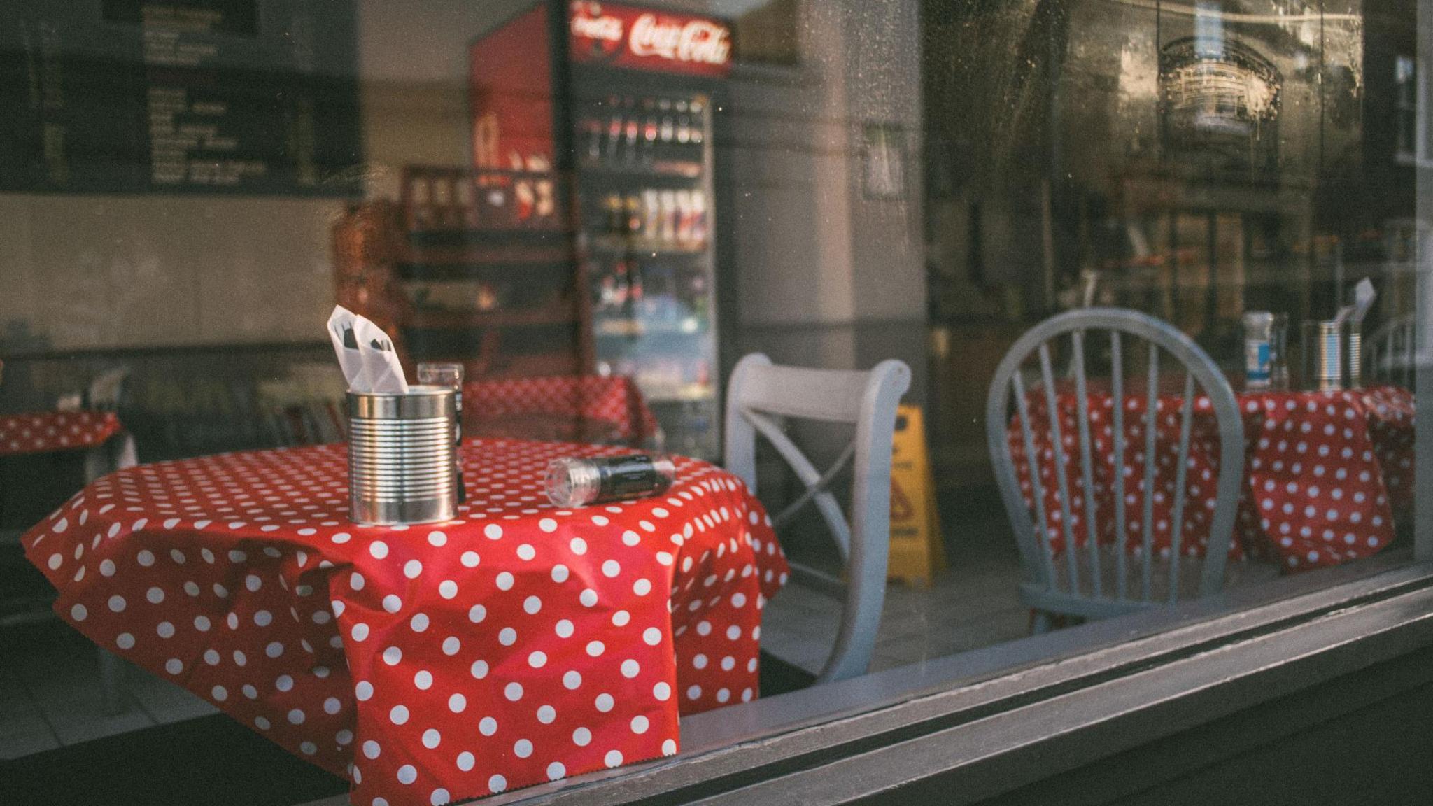 A set of restaurant tables with red and white dotted table cloths viewed through a window