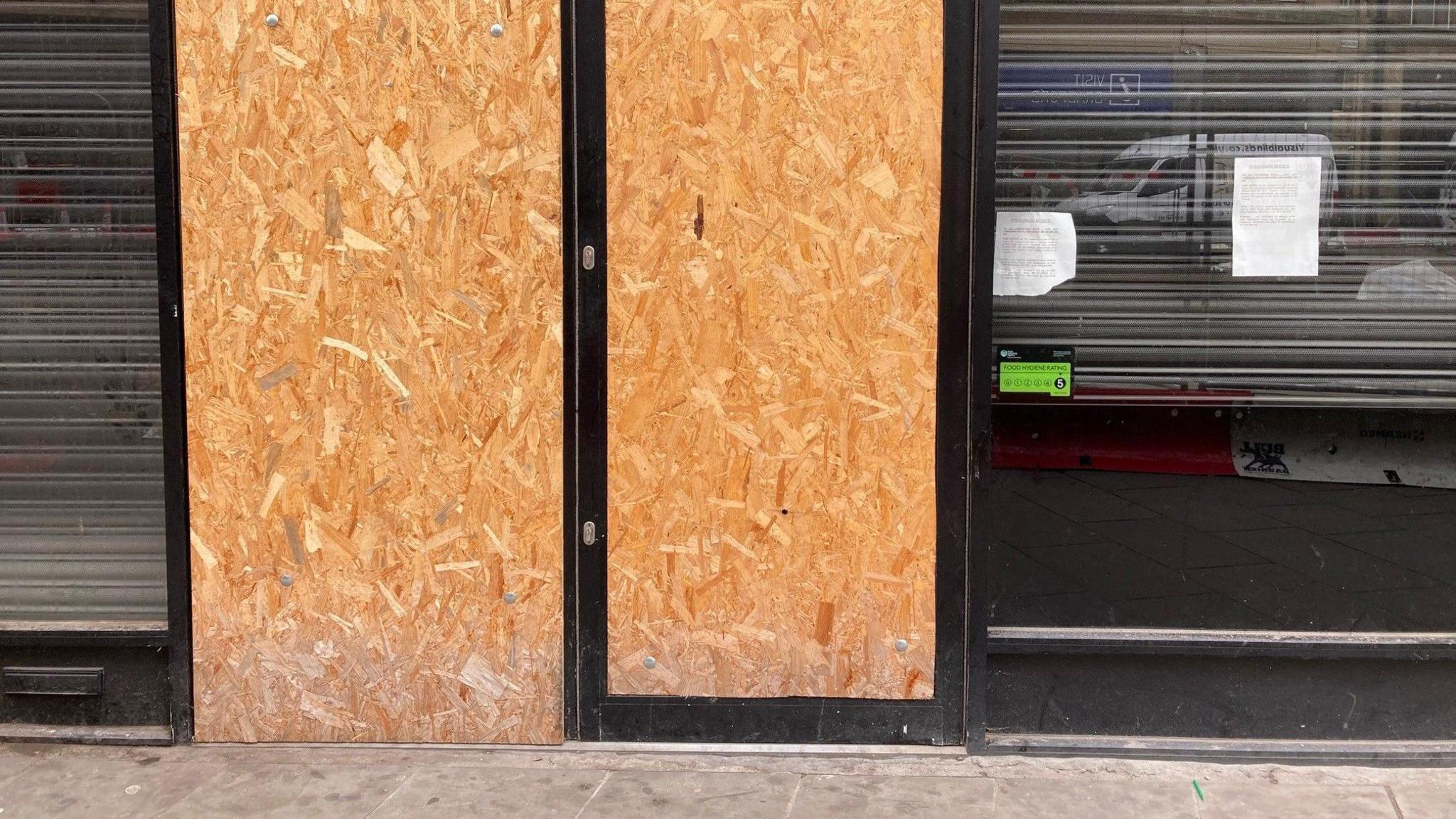 Two boarded up glass doors in the entrance to an empty shop on Broadway