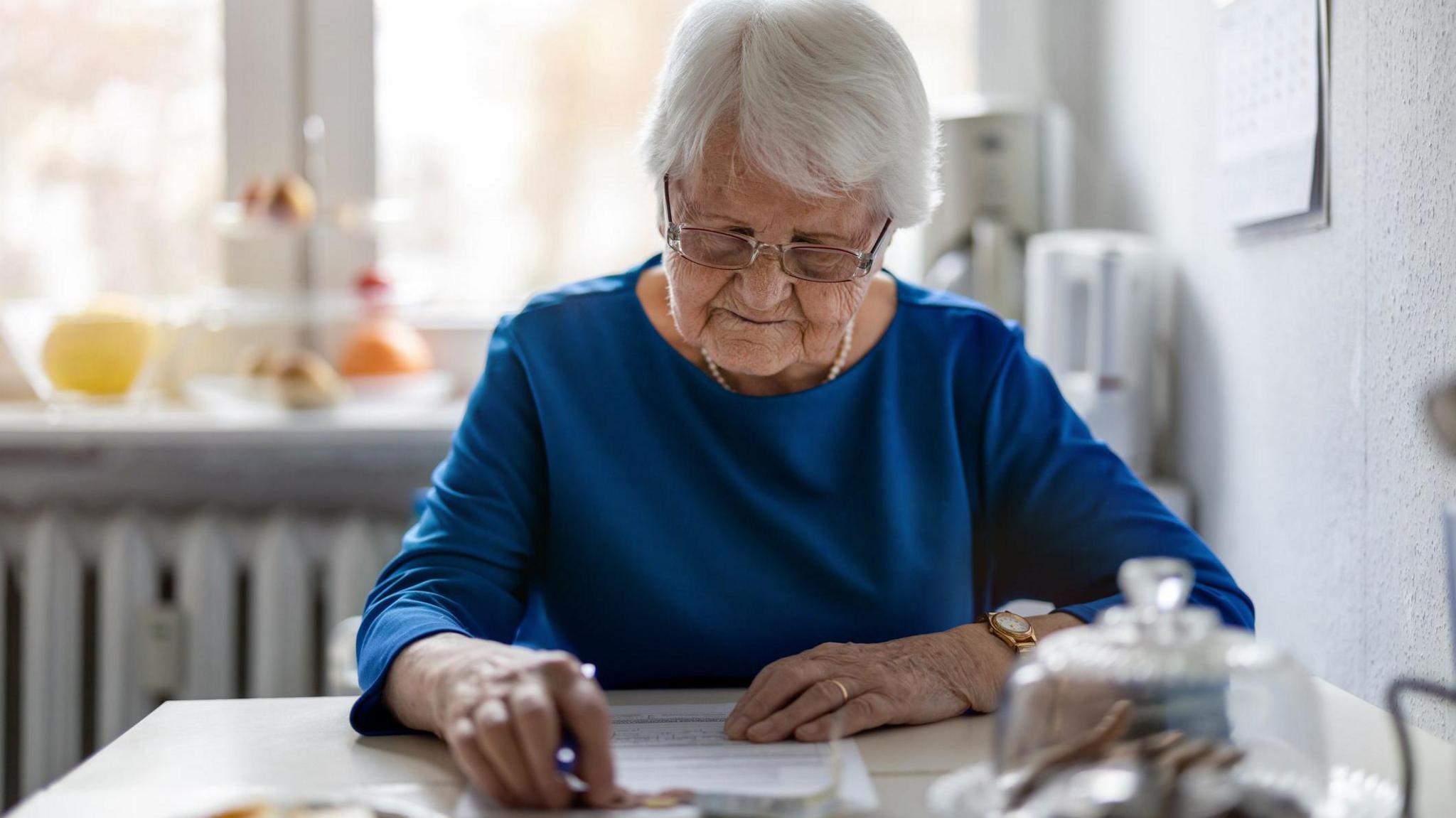 An elderly woman sitting at a table looks at a form