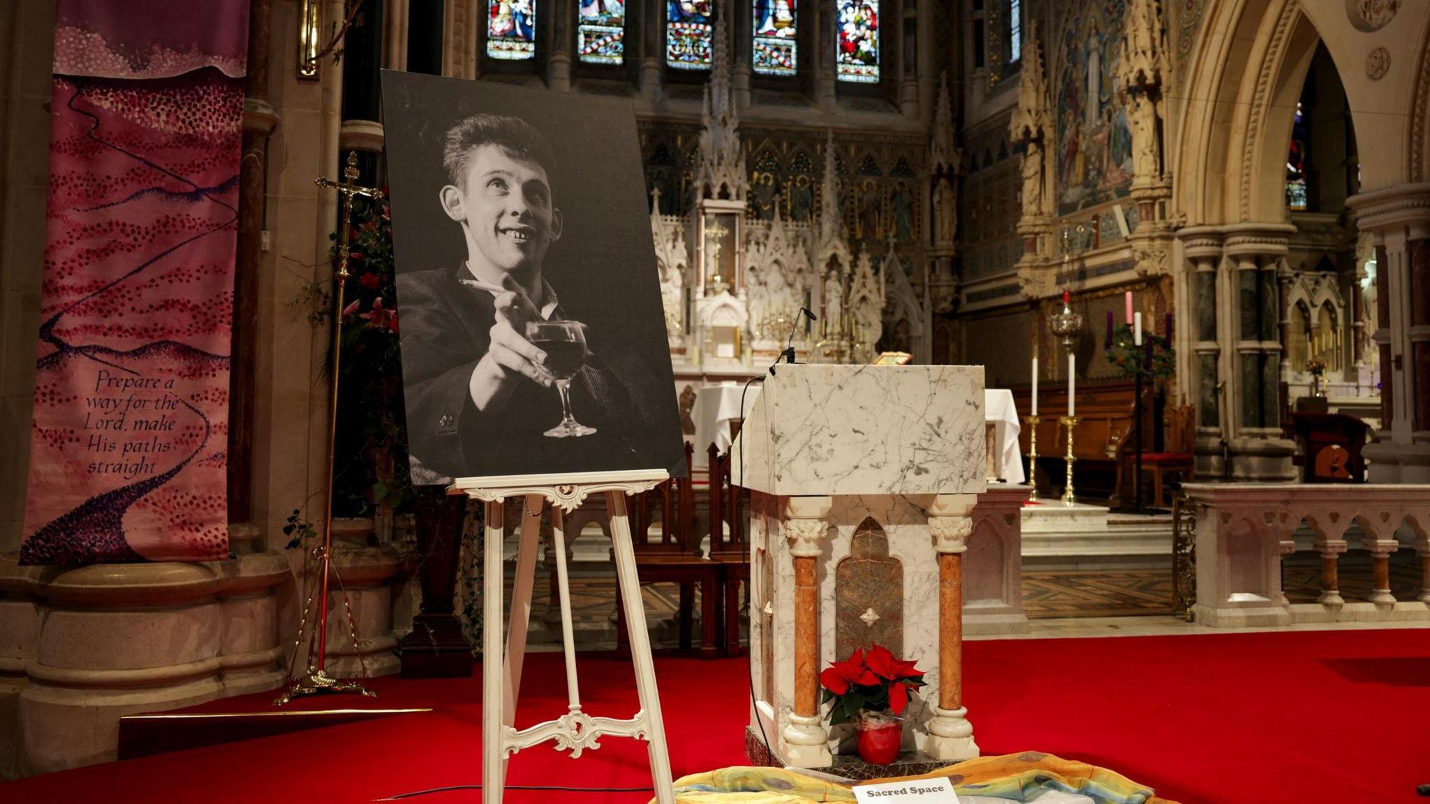 A black and white picture of Shane MacGowan holding a glass of wine at a church where his funeral took place