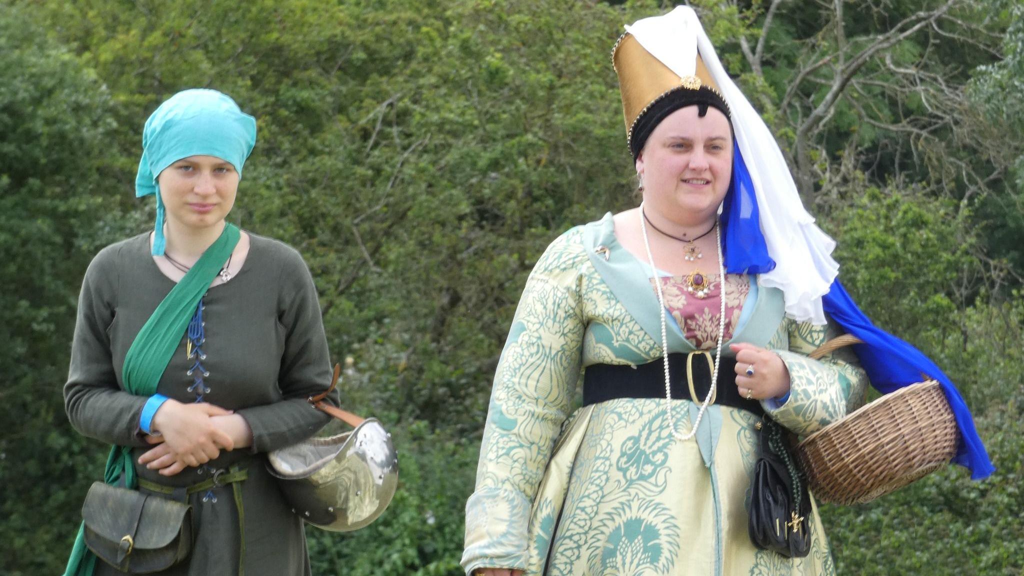 Two women walking with baskets wearing medieval dresses and head pieces