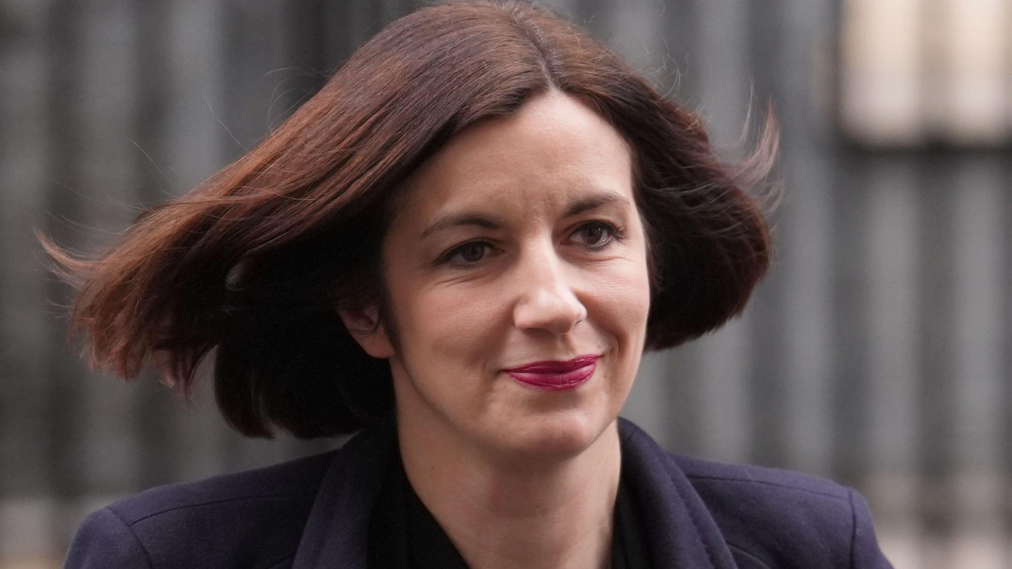 Bridget Phillipson is pictured walking out of Downing Street. She has short brown hair and is smiling. She wears a navy coloured coat.