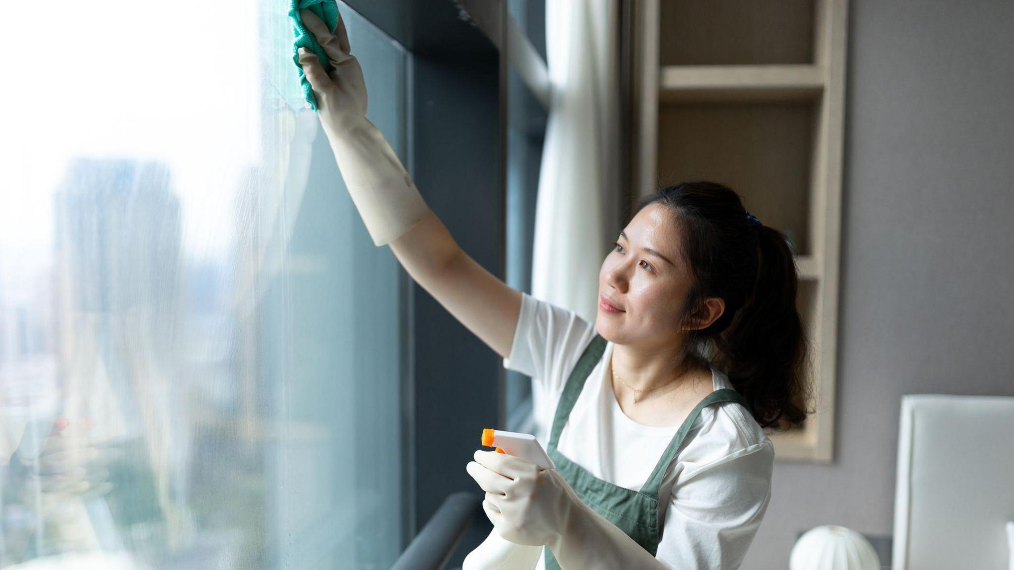 Woman in green apron cleaning a hotel room window