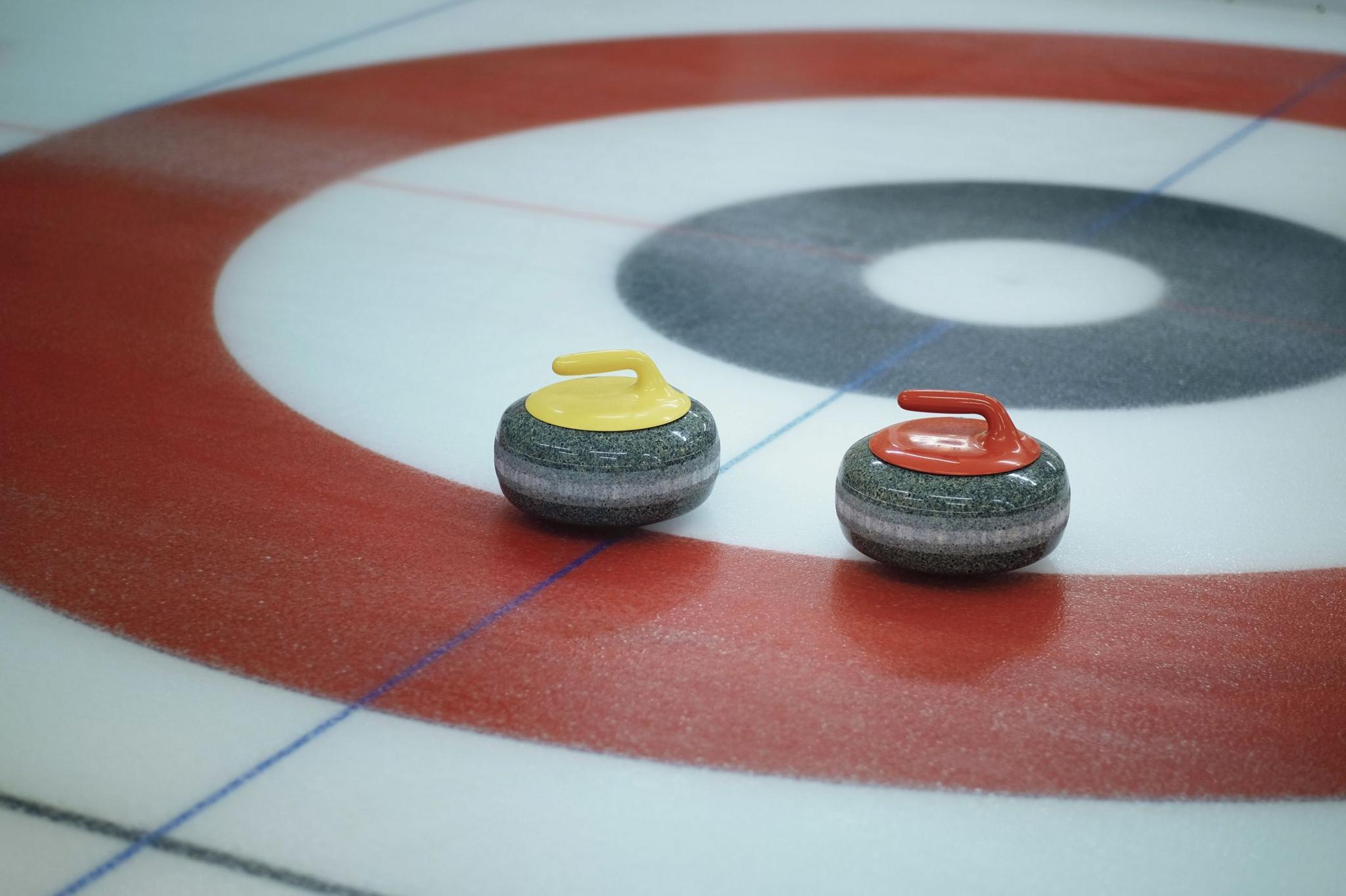 Two curling stones - one yellow, one red - on the ice at a rink during a curling match