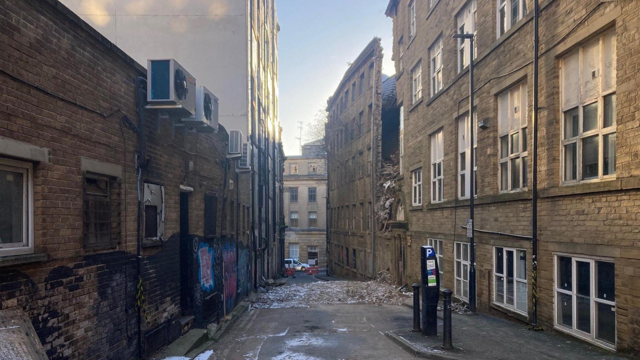 A street with stone buildings either side and flattened rubble across the road
